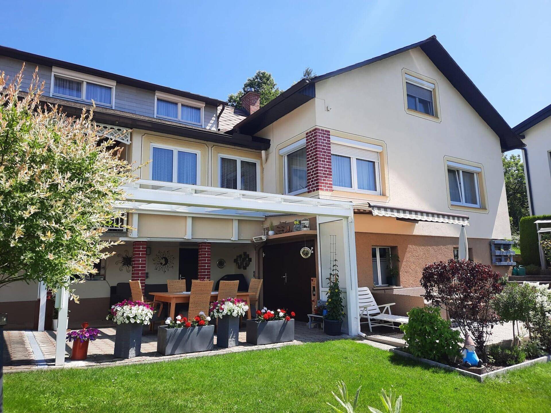 Gartenansicht des Hauses mit überdachter Terrasse, Esstisch und Blumenkübeln.