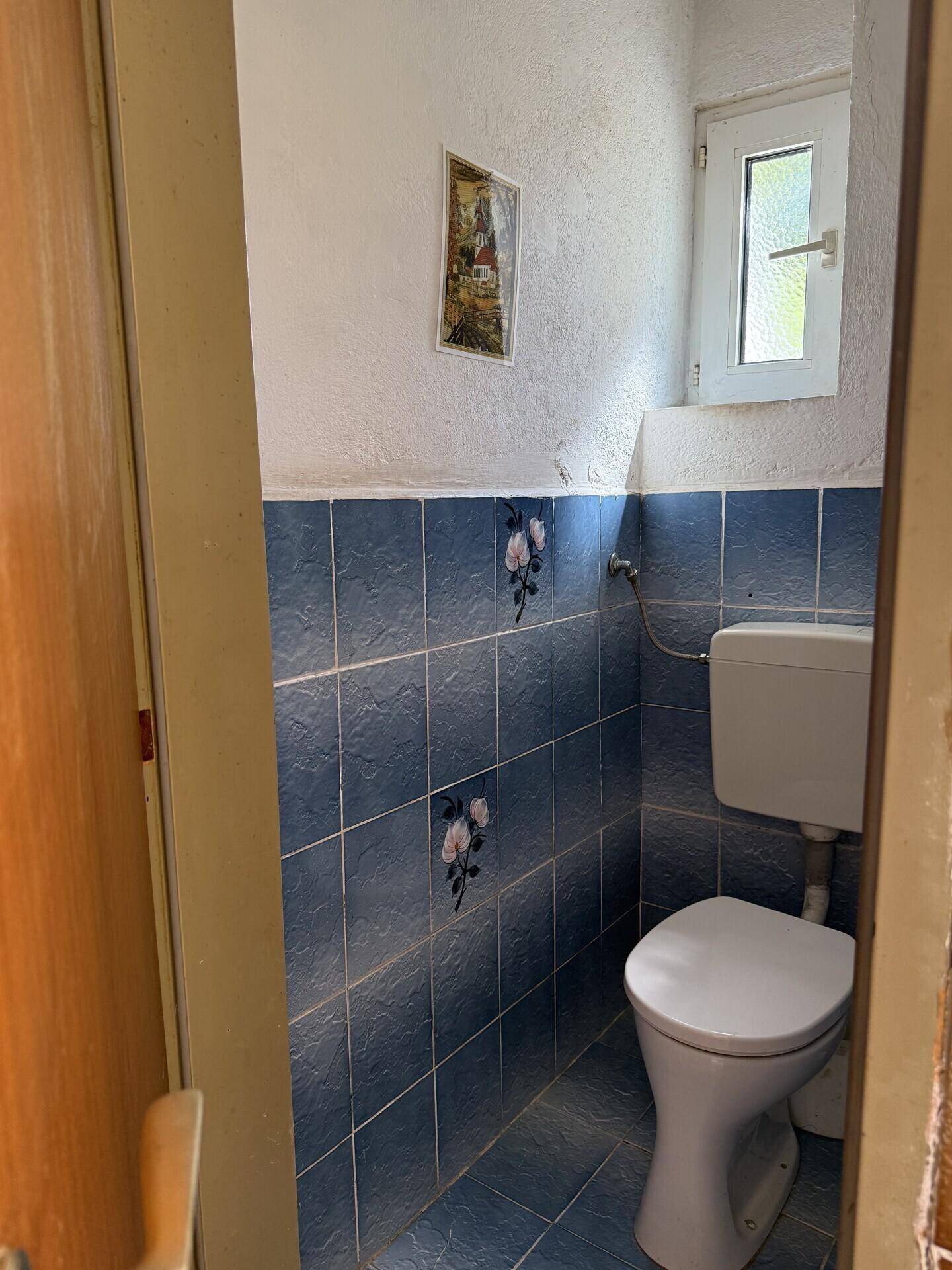 Kleines Gäste-WC mit blauen Fliesen, Toilette und einem kleinen Fenster für Belüftung.