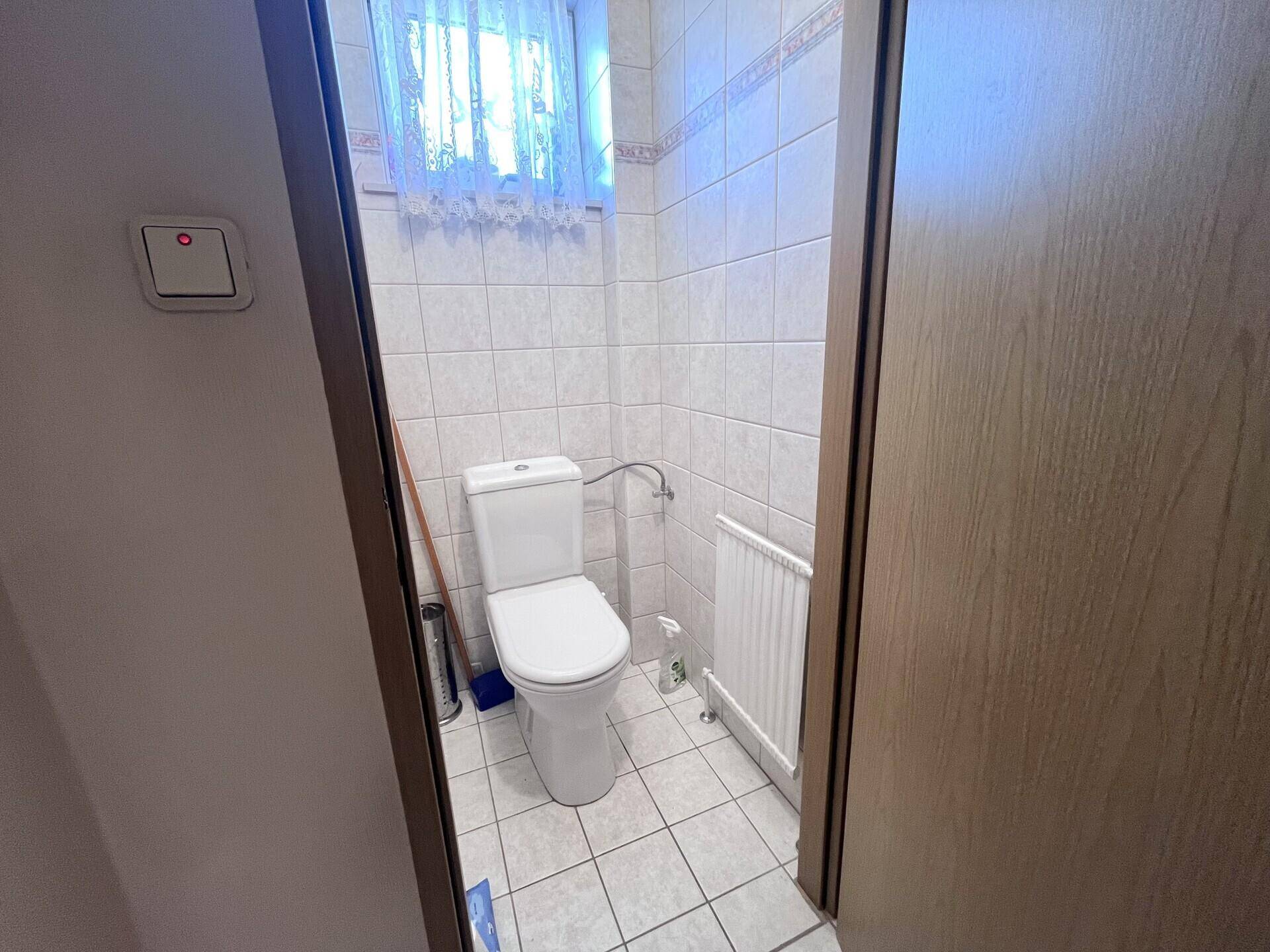 Kleines Gäste-WC mit Toilette, Heizkörper und vollständig gefliesten Wänden und Boden.