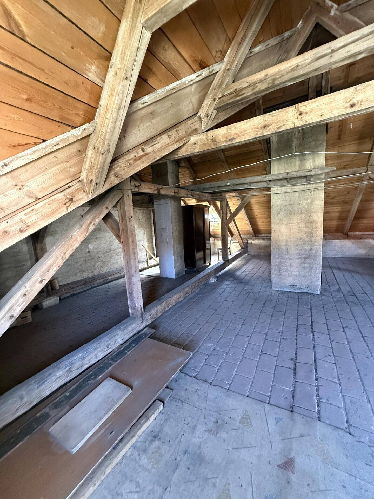 Geräumiger Dachboden mit sichtbaren Holzbalken und Ziegelboden, bereit für den Ausbau.