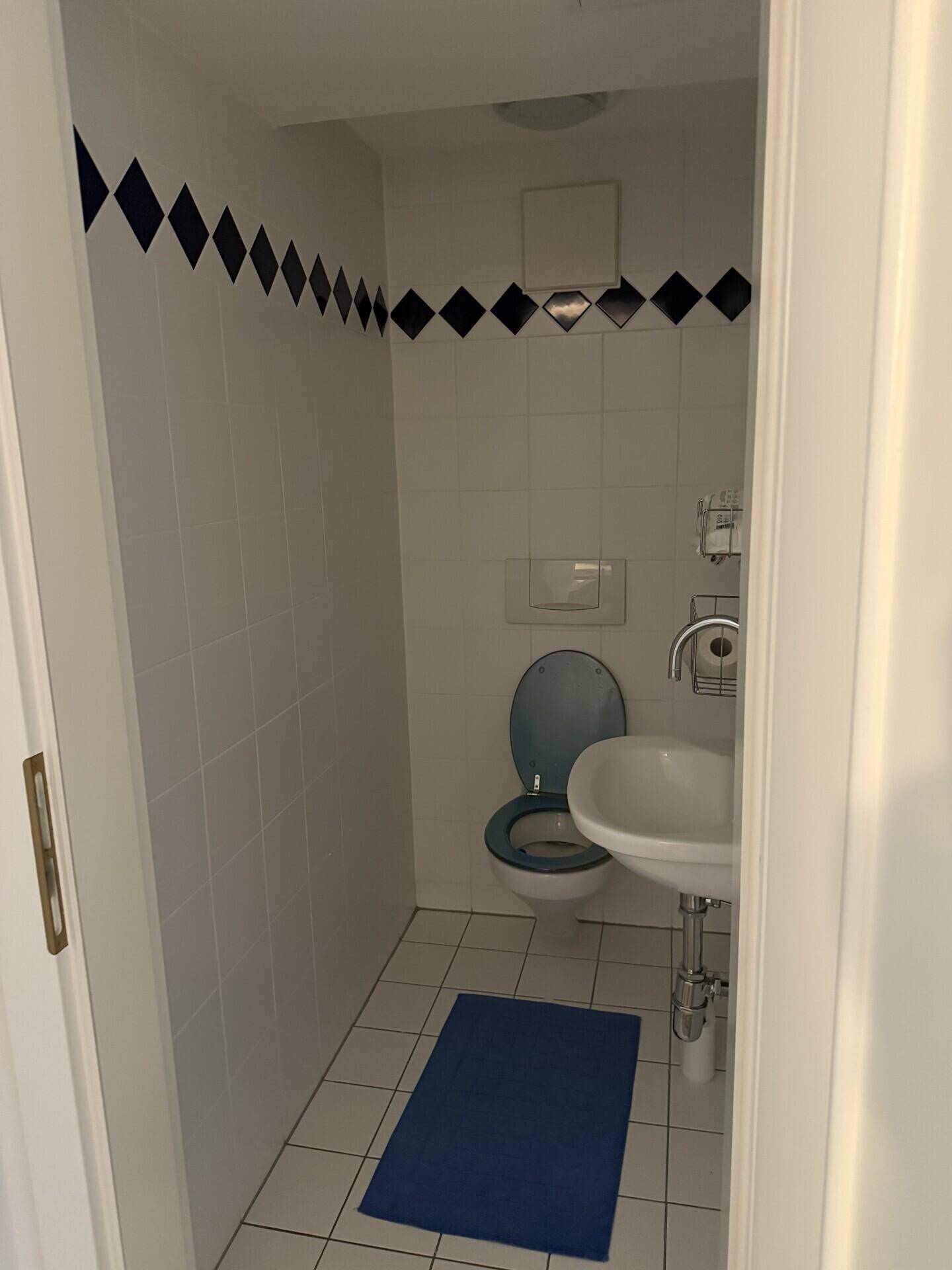 Kleines WC mit weißen Fliesen, blauen Akzenten und Waschbecken.