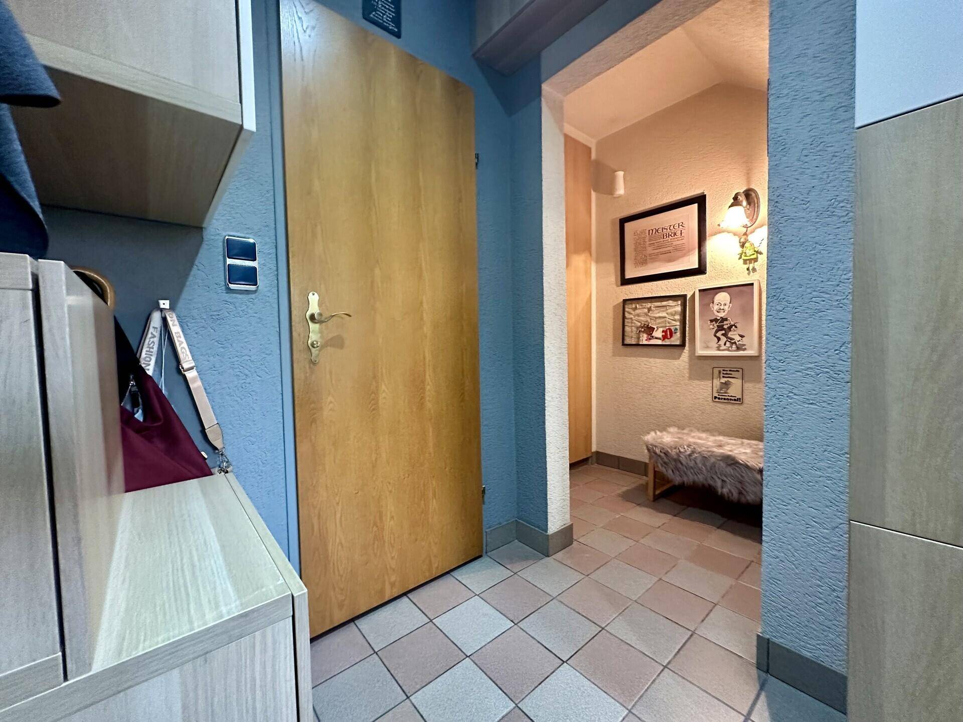 Detailansicht einer Holztür im Flur mit Wanddekorationen und Fliesenboden.
