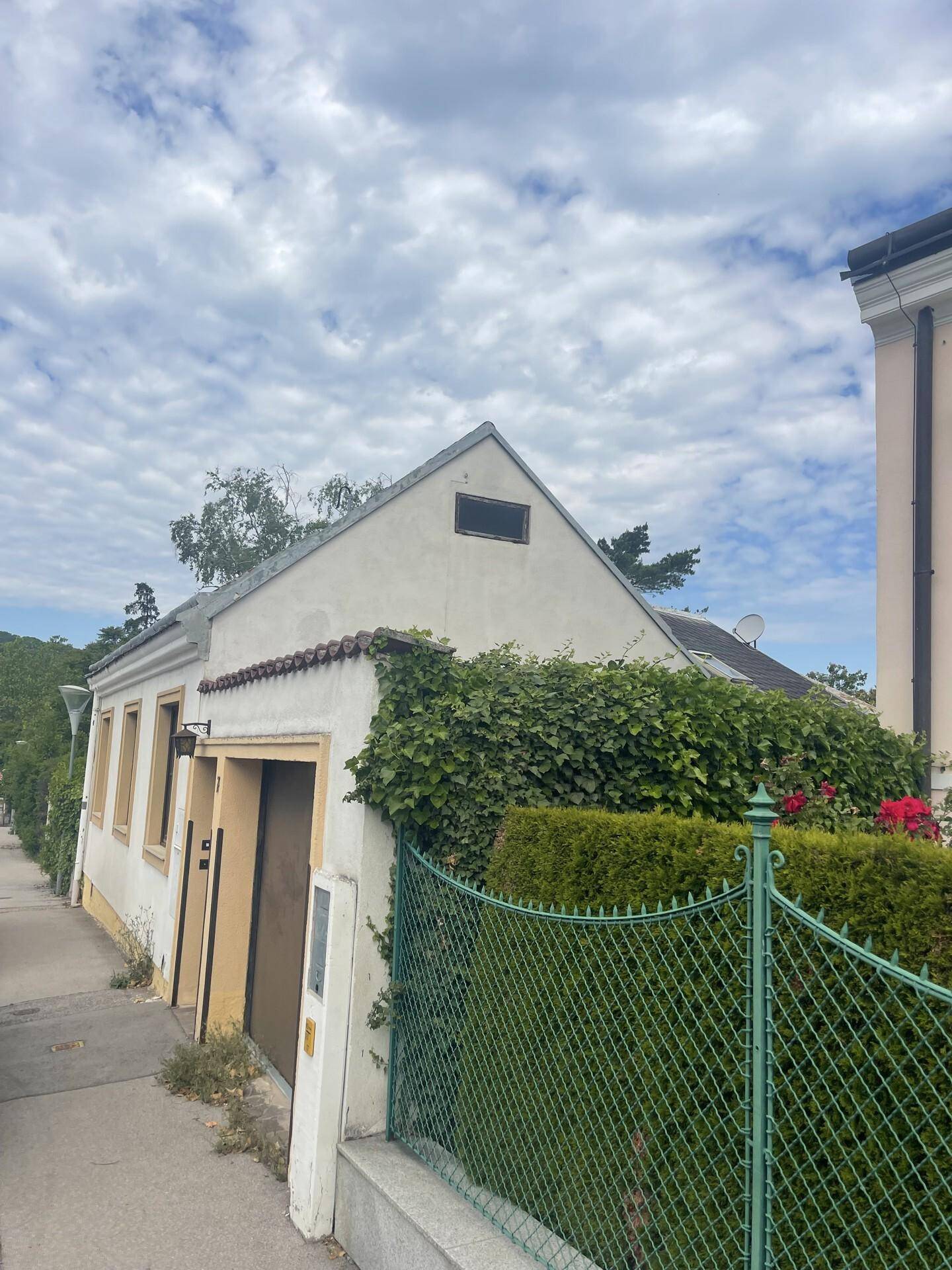 Weißes Haus mit Satteldach und Efeu an der Fassade, von der Straße aus gesehen.