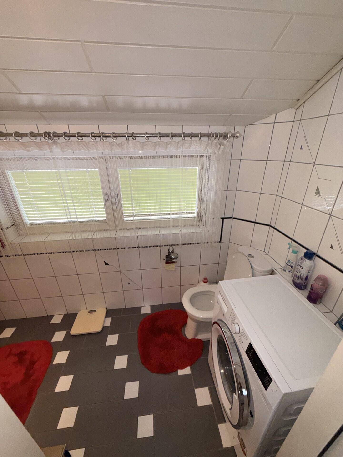Dachgeschoss-Badezimmer mit Dachschrägen, weißen Fliesen und Waschmaschine.