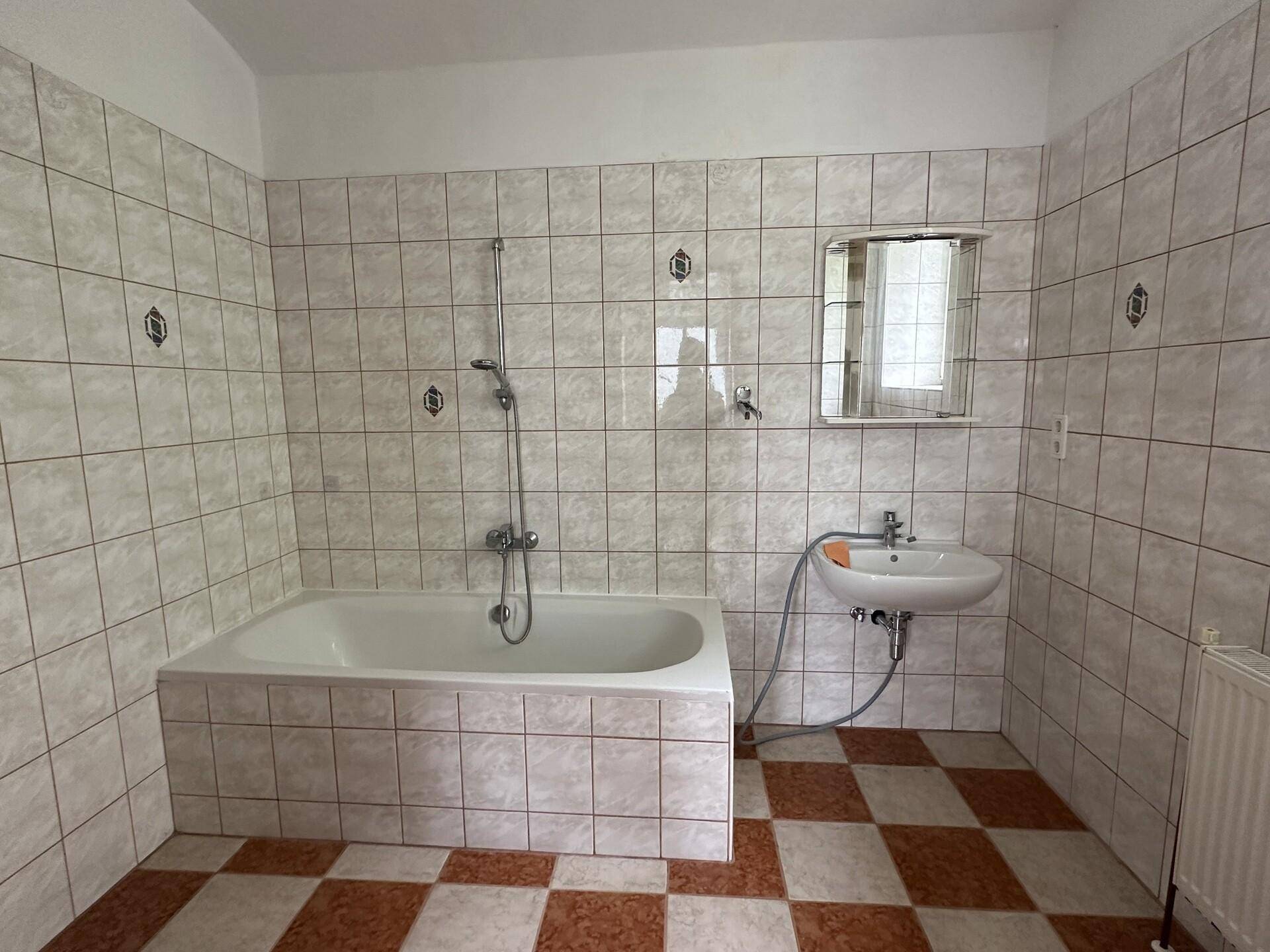 Badezimmer mit Badewanne, Waschbecken und weiß-braun kariertem Fliesenboden.