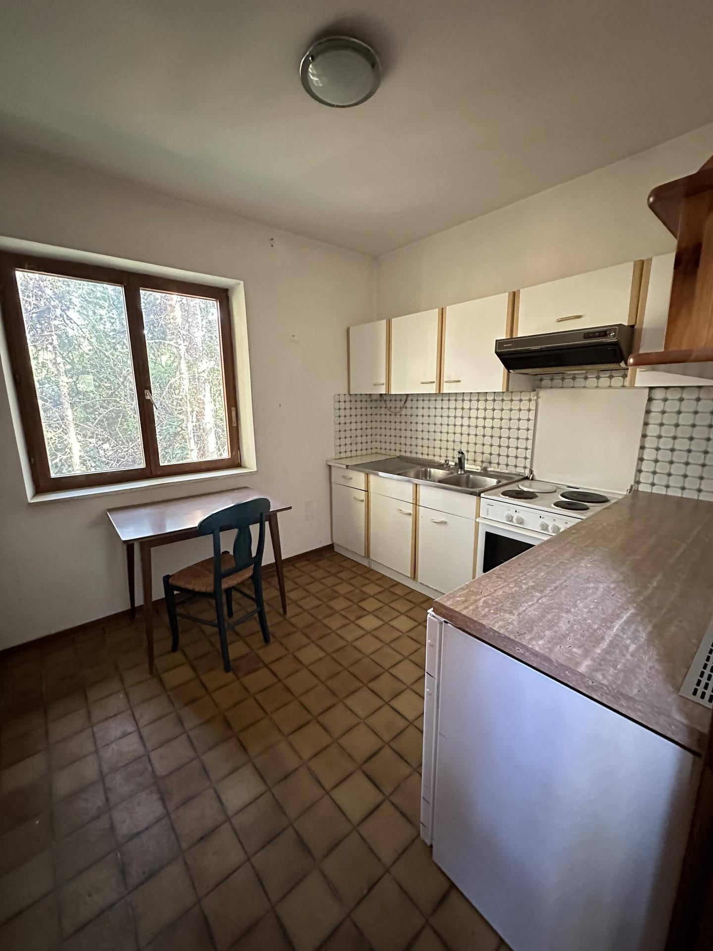 Kleine Küche mit weißen Schränken, Elektroherd und Kühlschrank, ausgestattet mit einem Esstisch und Stuhl.