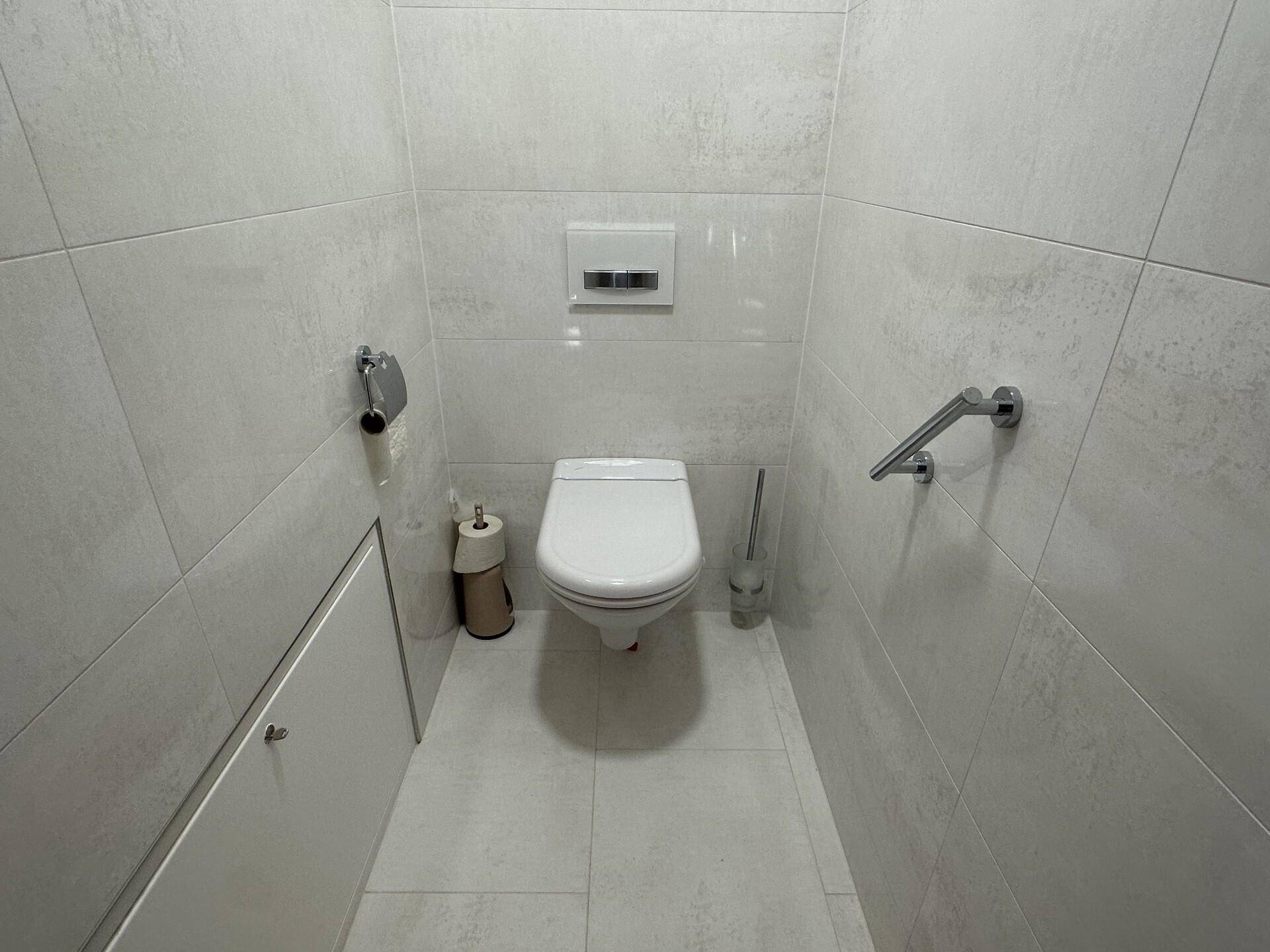 Kleines WC mit wandhängender Toilette, Haltegriffen und hellen Fliesen.