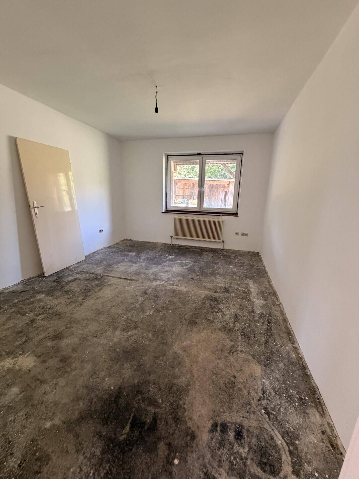 Leeres Zimmer mit weißen Wänden, Fenster und Heizkörper, bereit für Renovierung.