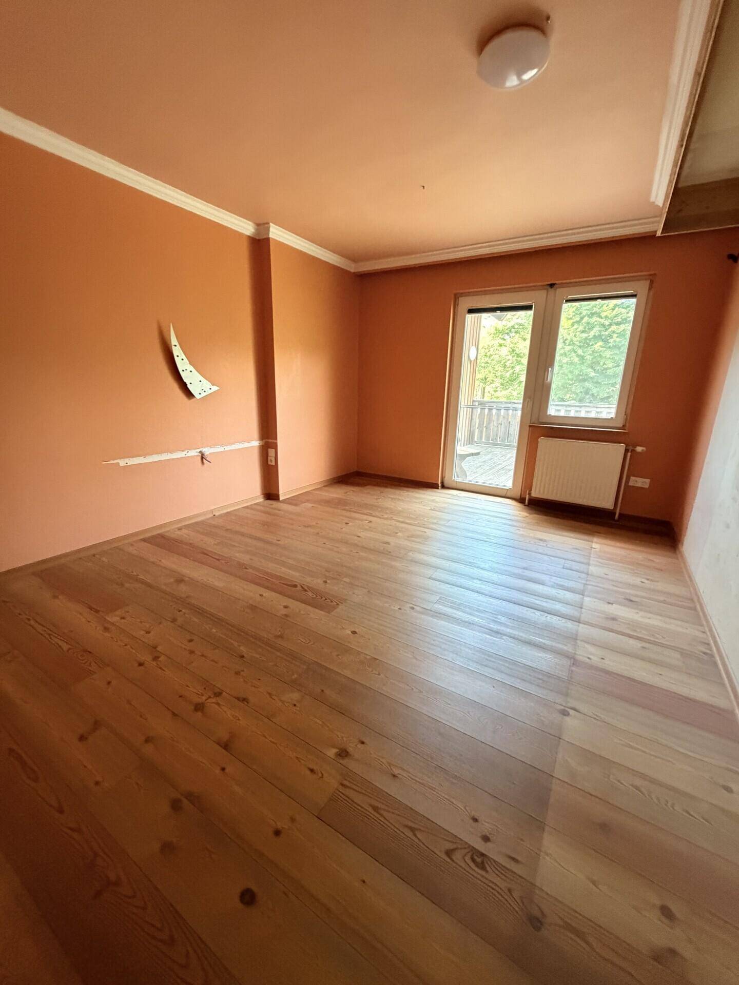 Schlafzimmer mit Holzboden, orangefarbenen Wänden und Zugang zu einem Balkon.