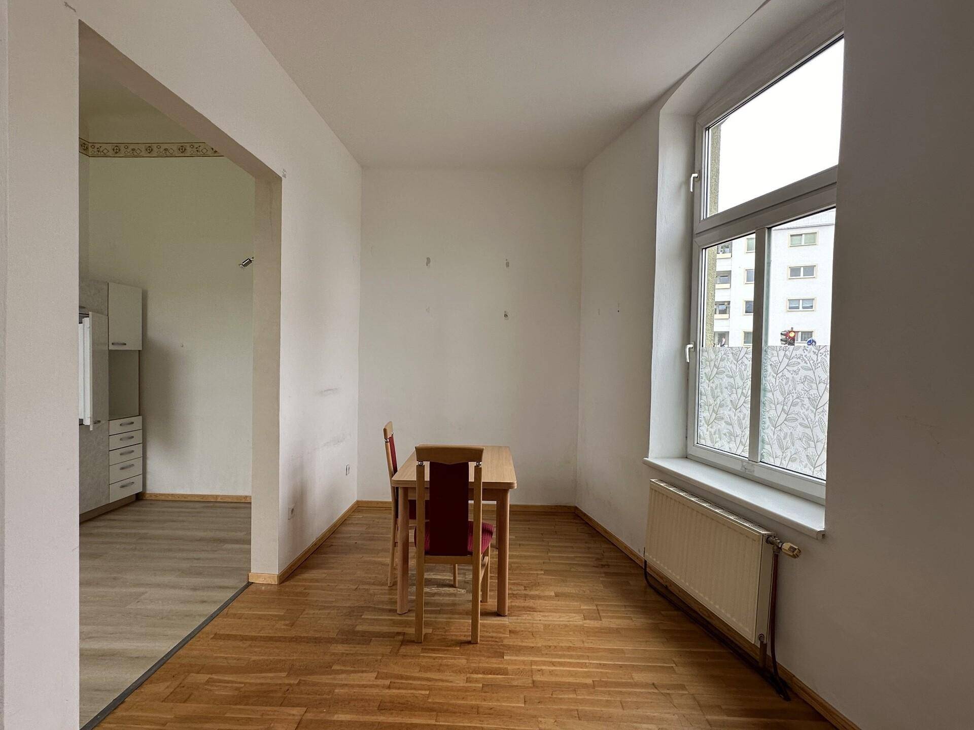 Essbereich mit Holztisch und Stühlen, angrenzend an die Küche, mit Parkettboden und Fenster.
