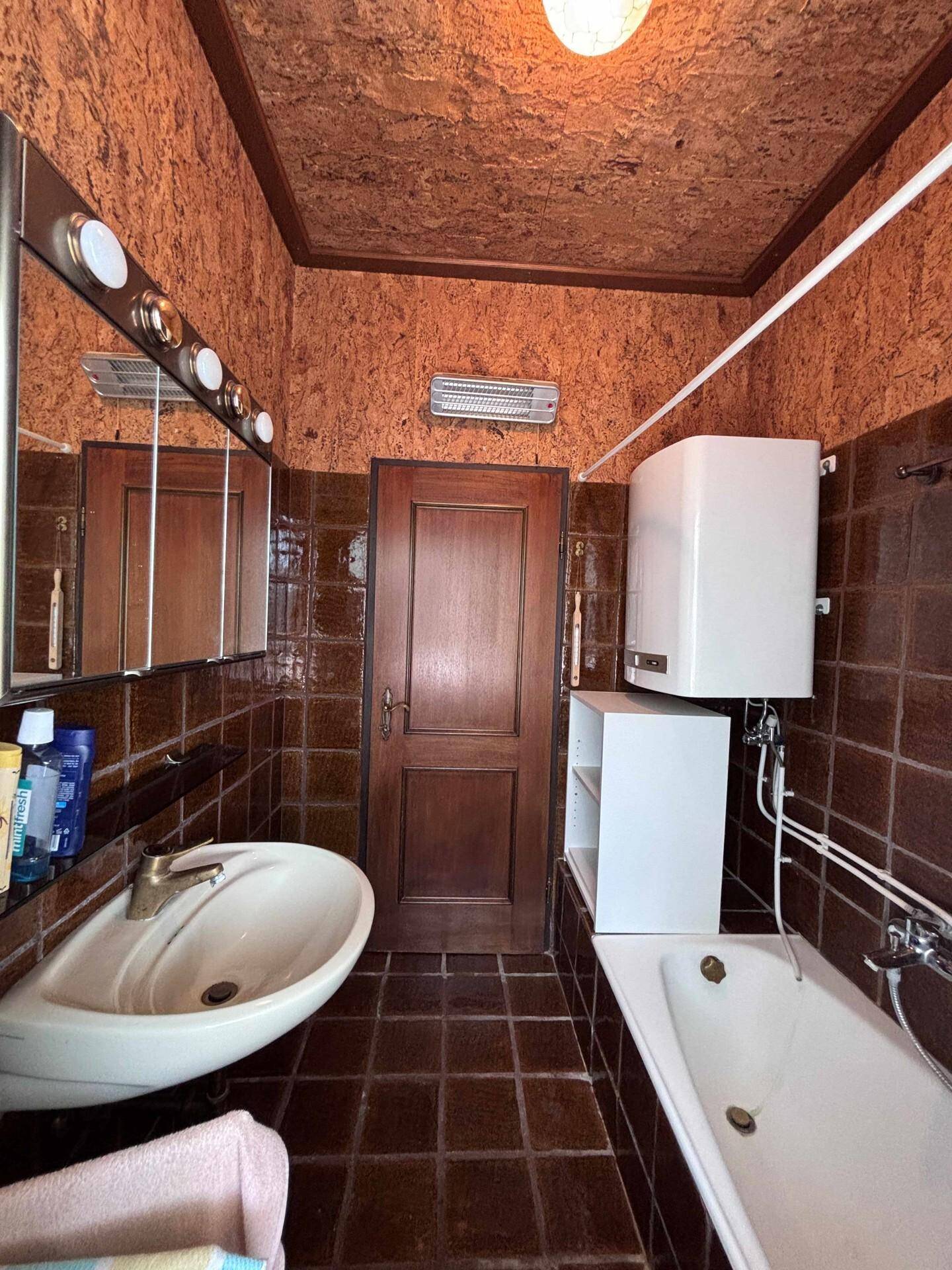 Badezimmer mit braunen Fliesen, Badewanne, Waschbecken und Spiegelschrank.