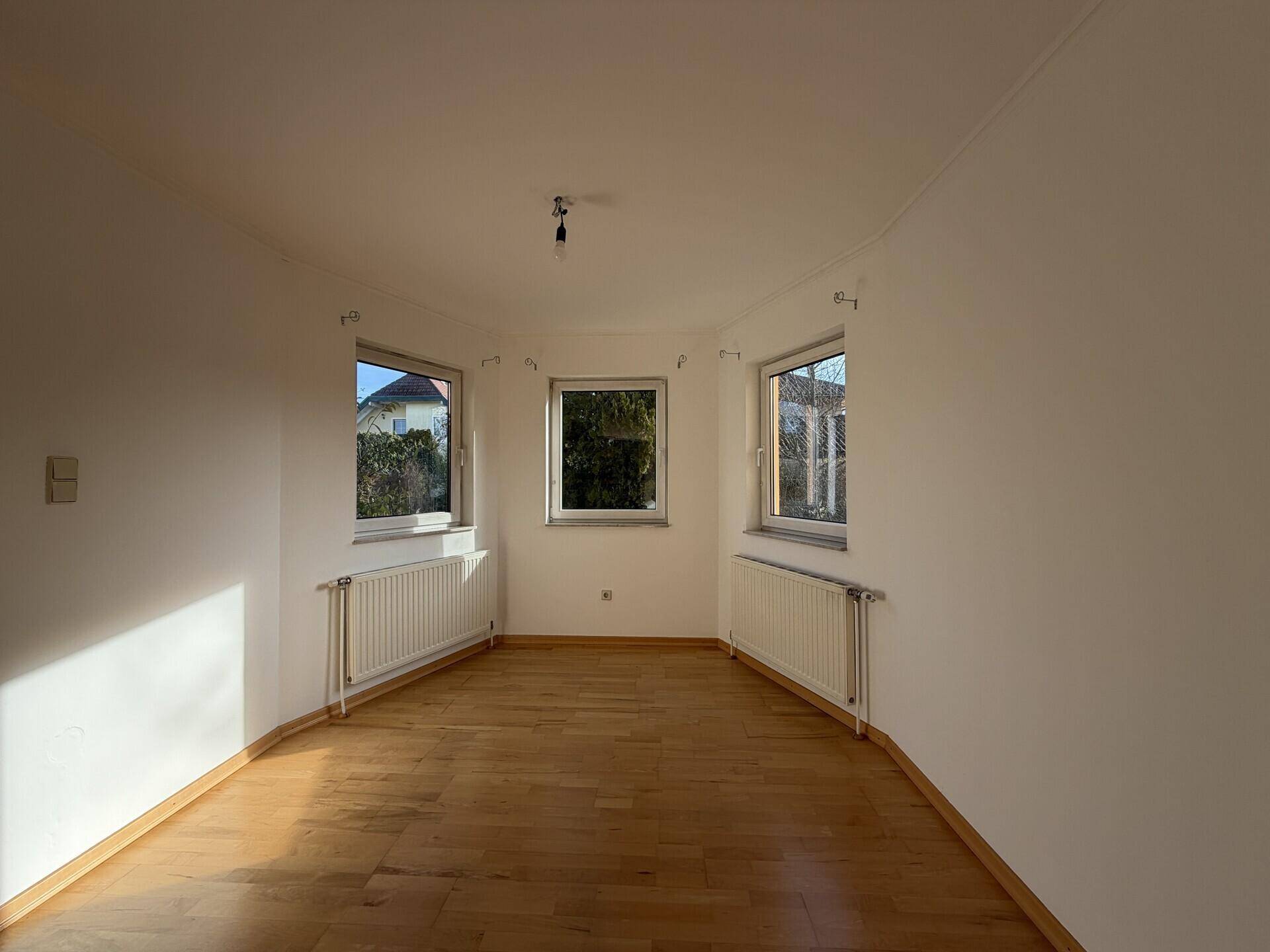 Heller Raum mit Parkettboden und drei Fenstern, die viel Tageslicht hereinlassen.