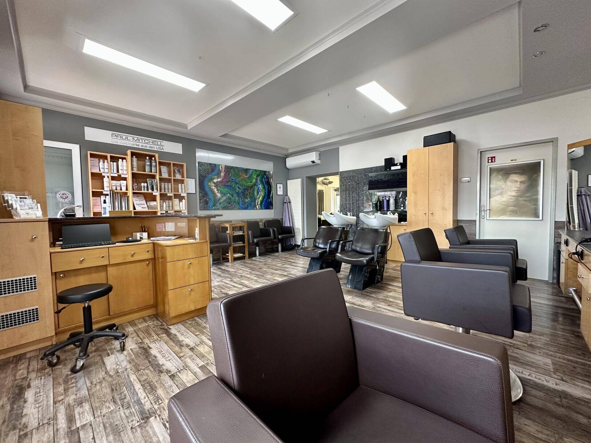 Empfangsbereich und weitere Styling-Stühle in einem modernen Friseursalon mit Holzmöbeln.