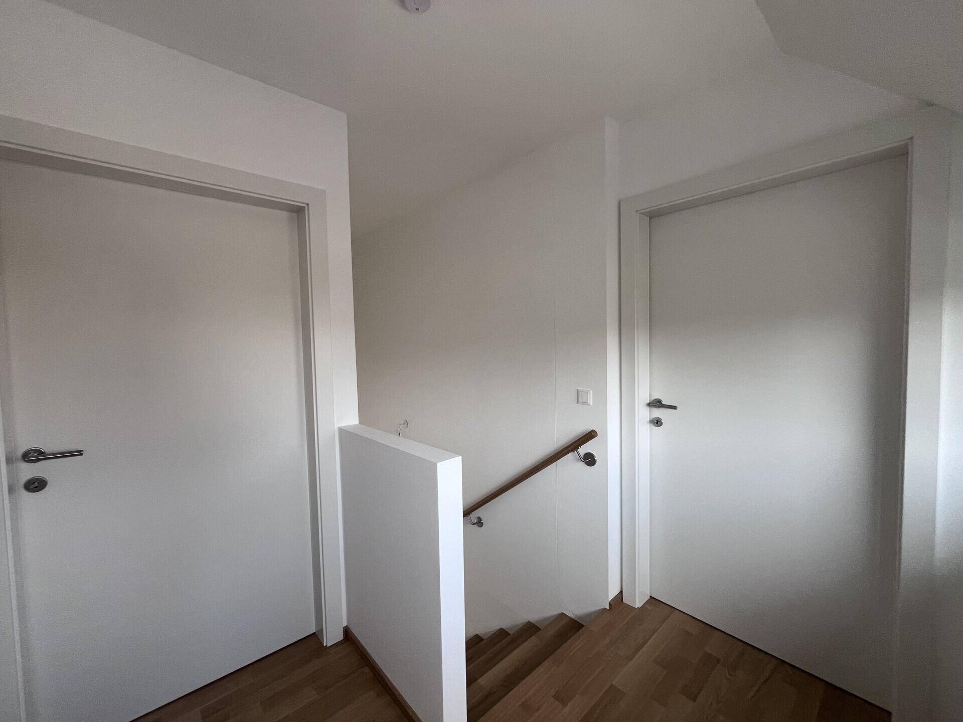 Treppenhaus mit Holzgeländer und weißen Wänden, das zu den oberen Etagen führt.