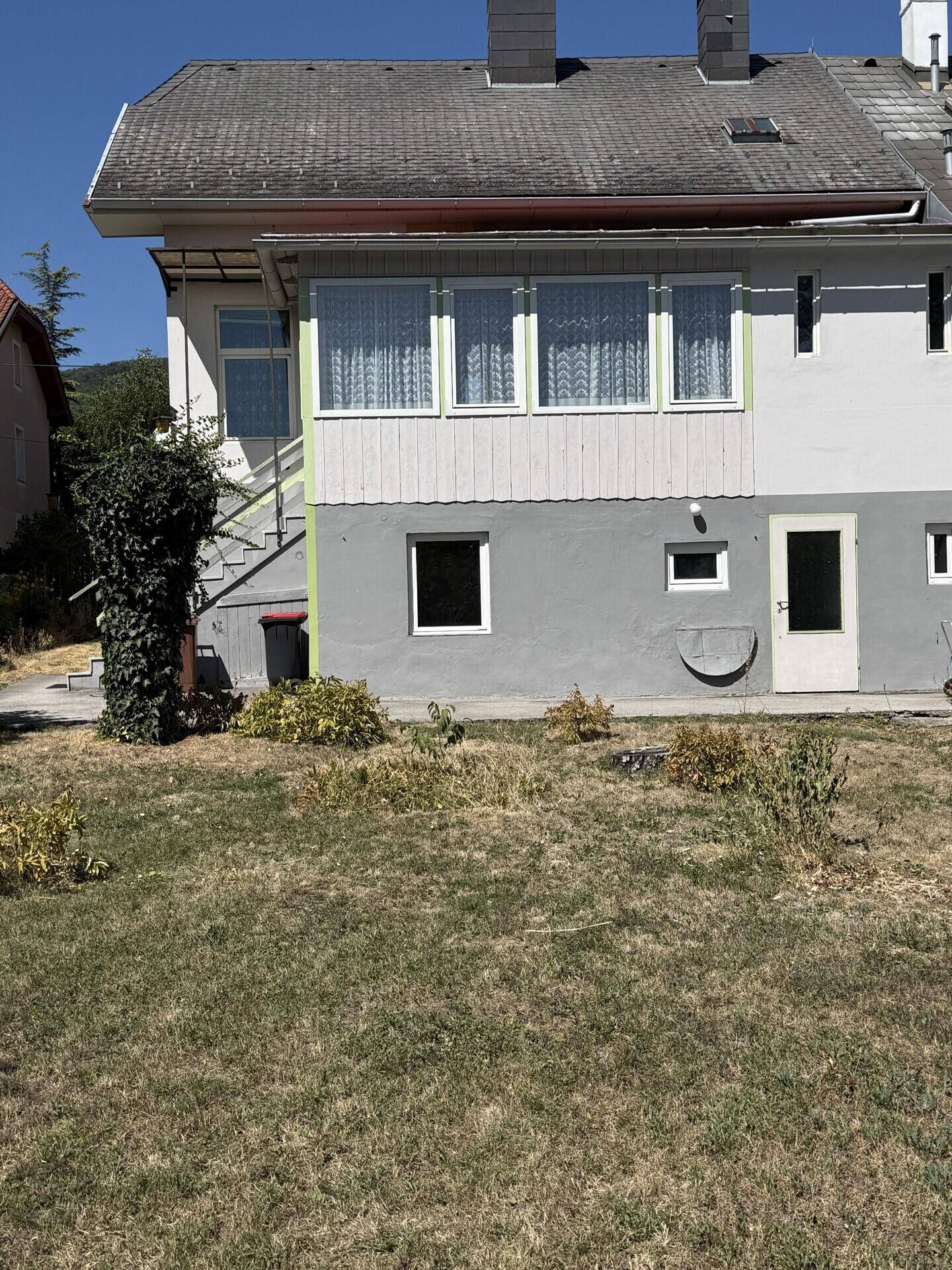 Weitläufiger Gartenbereich hinter dem Haus mit trockenem Rasen und Blick auf die Gebäuderückseite.