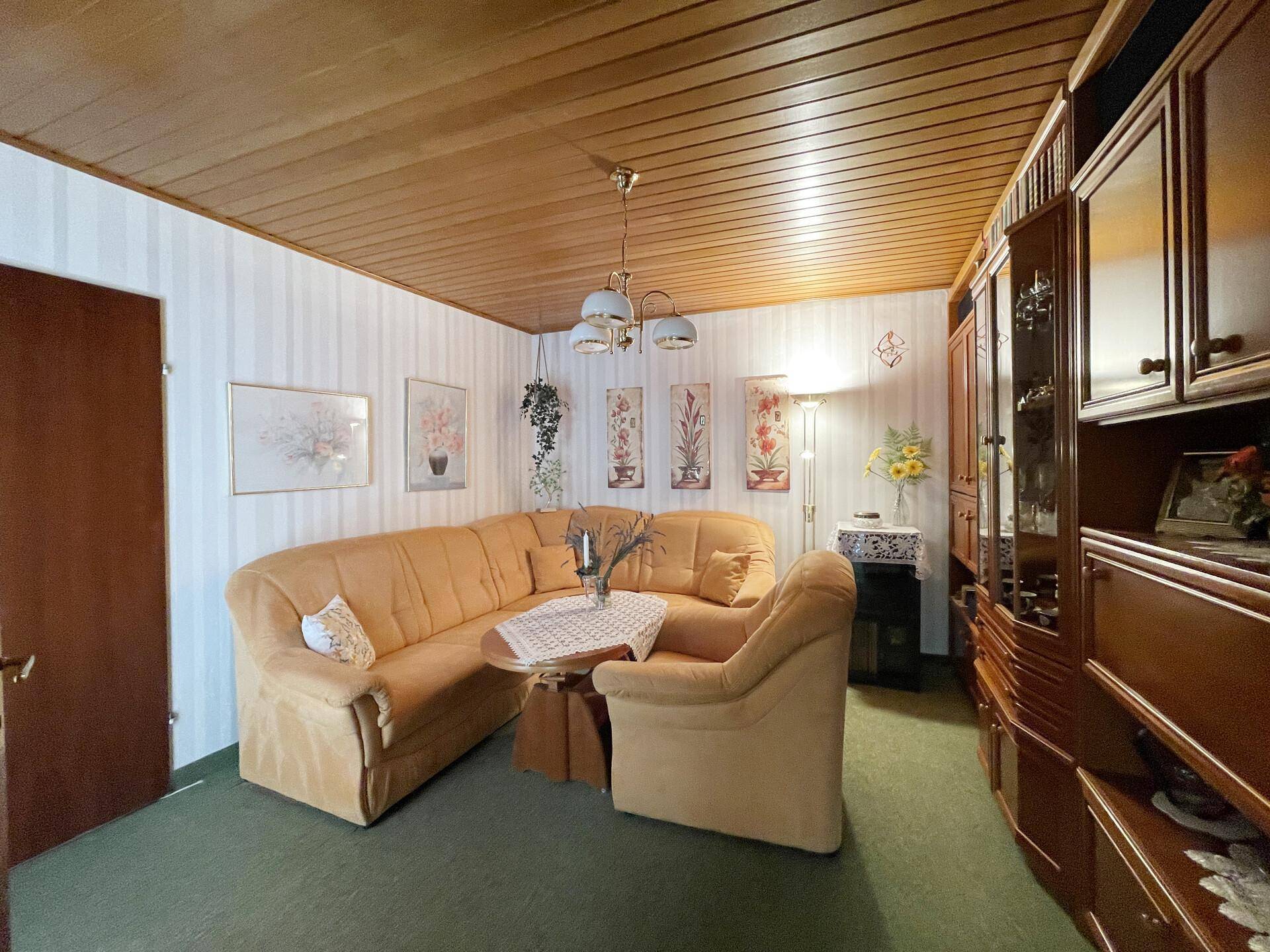 Geräumiges Wohnzimmer mit Ecksofa, Holzdecke und Teppichboden.