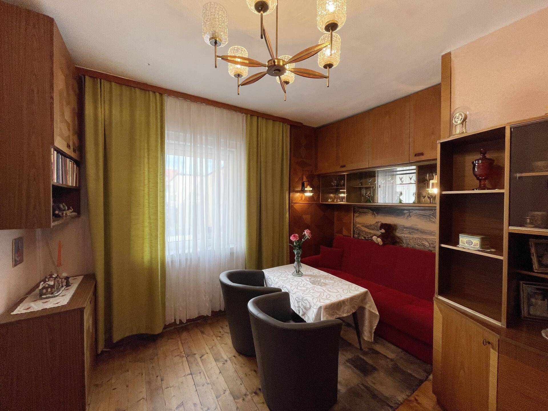 Helles Wohnzimmer mit Holzdielenboden, grünen Vorhängen und einem Esstisch.