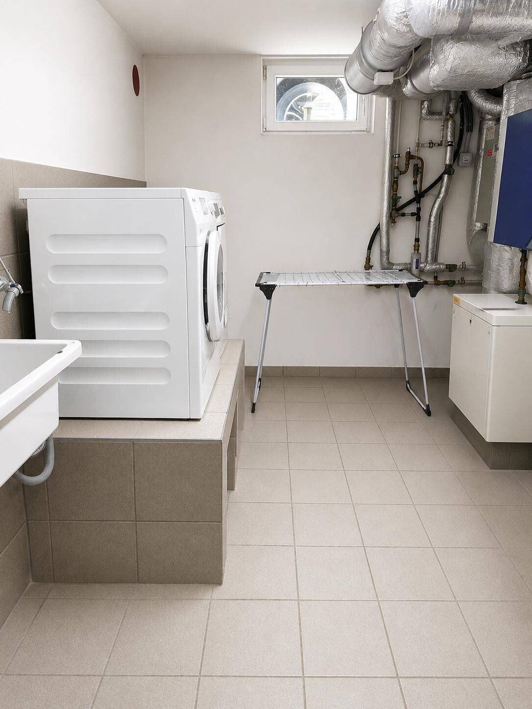 Praktischer Hauswirtschaftsraum im Keller mit Waschmaschine, Spülbecken und sichtbaren Installationen.