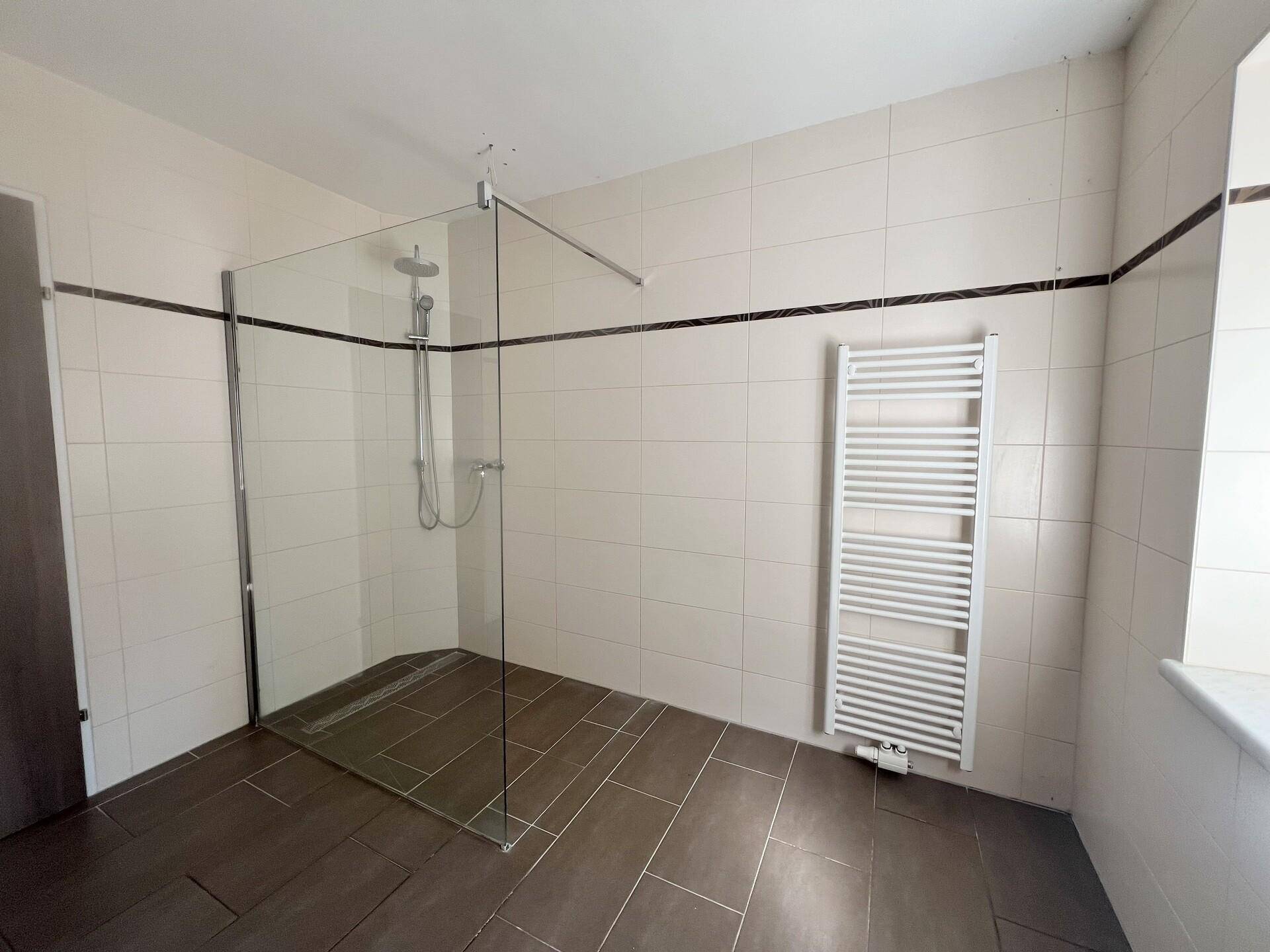 Badezimmer mit großer begehbarer Dusche, Handtuchheizkörper und Fliesenboden.