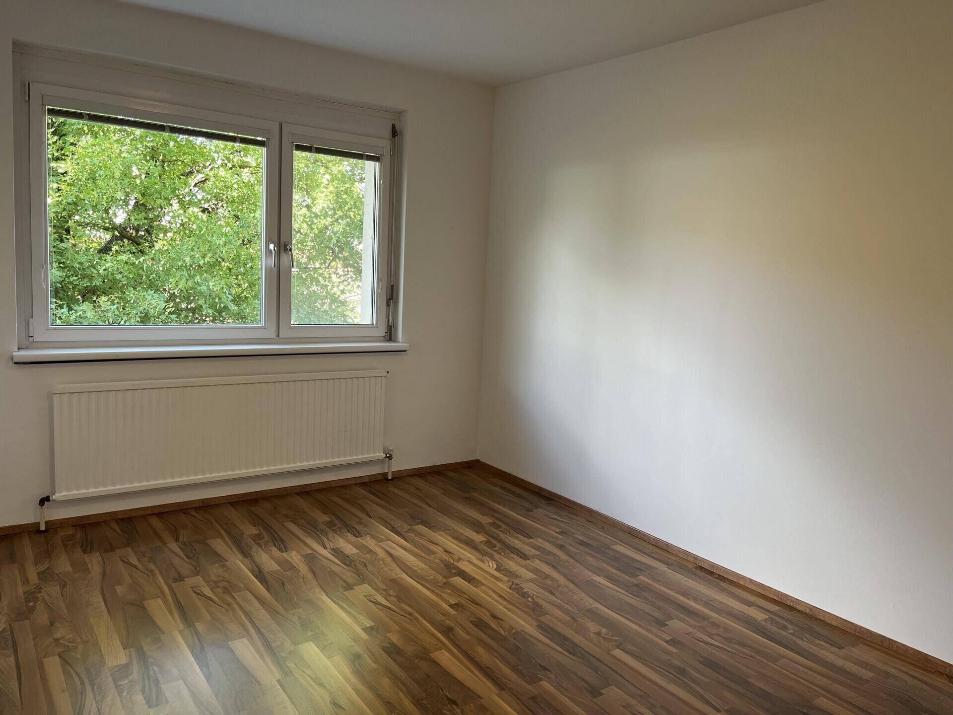 Freundlicher Raum mit dunklerem Laminatboden und Fenster mit Blick auf üppiges Grün.
