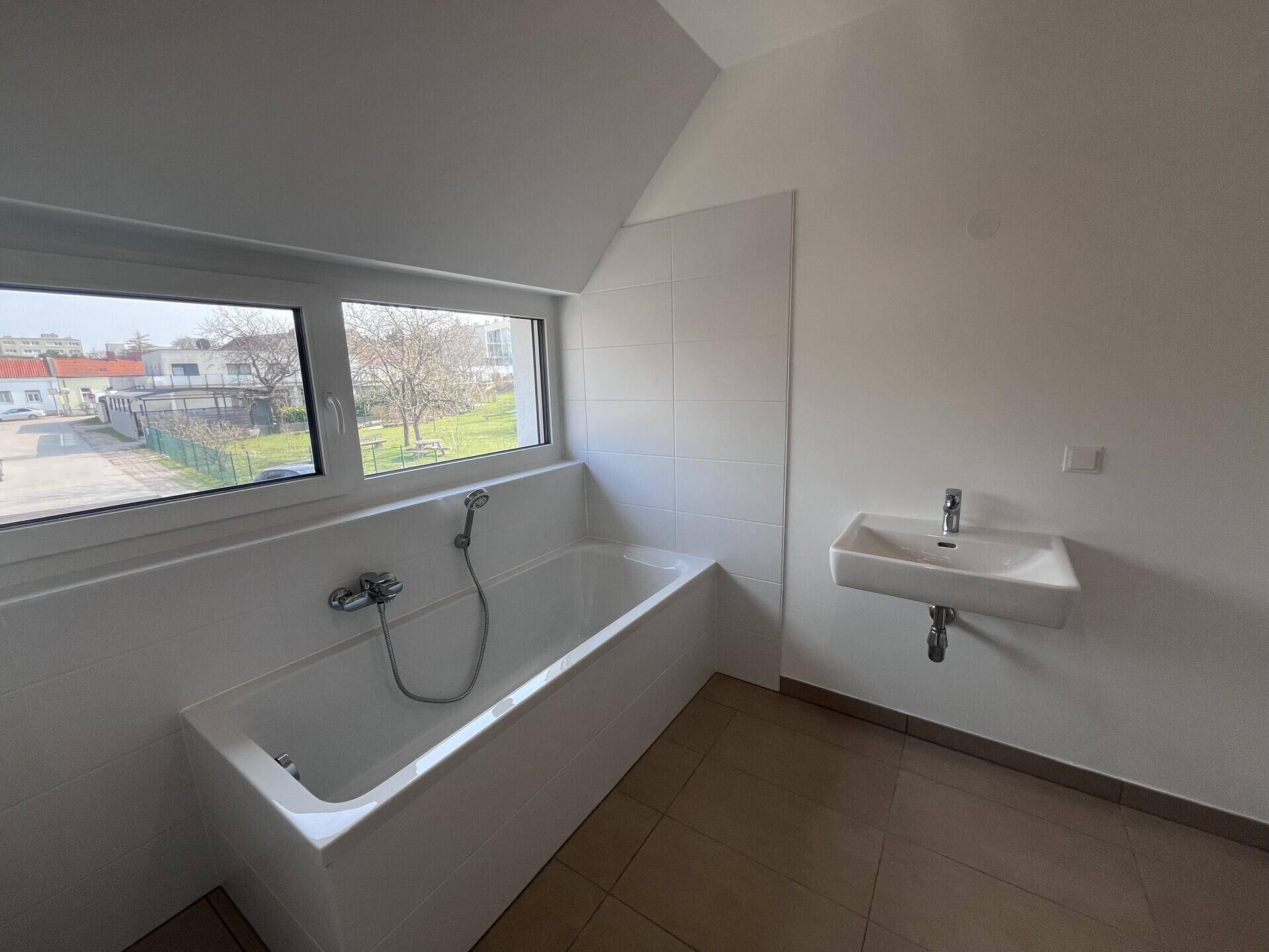 Helles Badezimmer mit Badewanne, Waschbecken und Fenster für natürliche Belüftung.