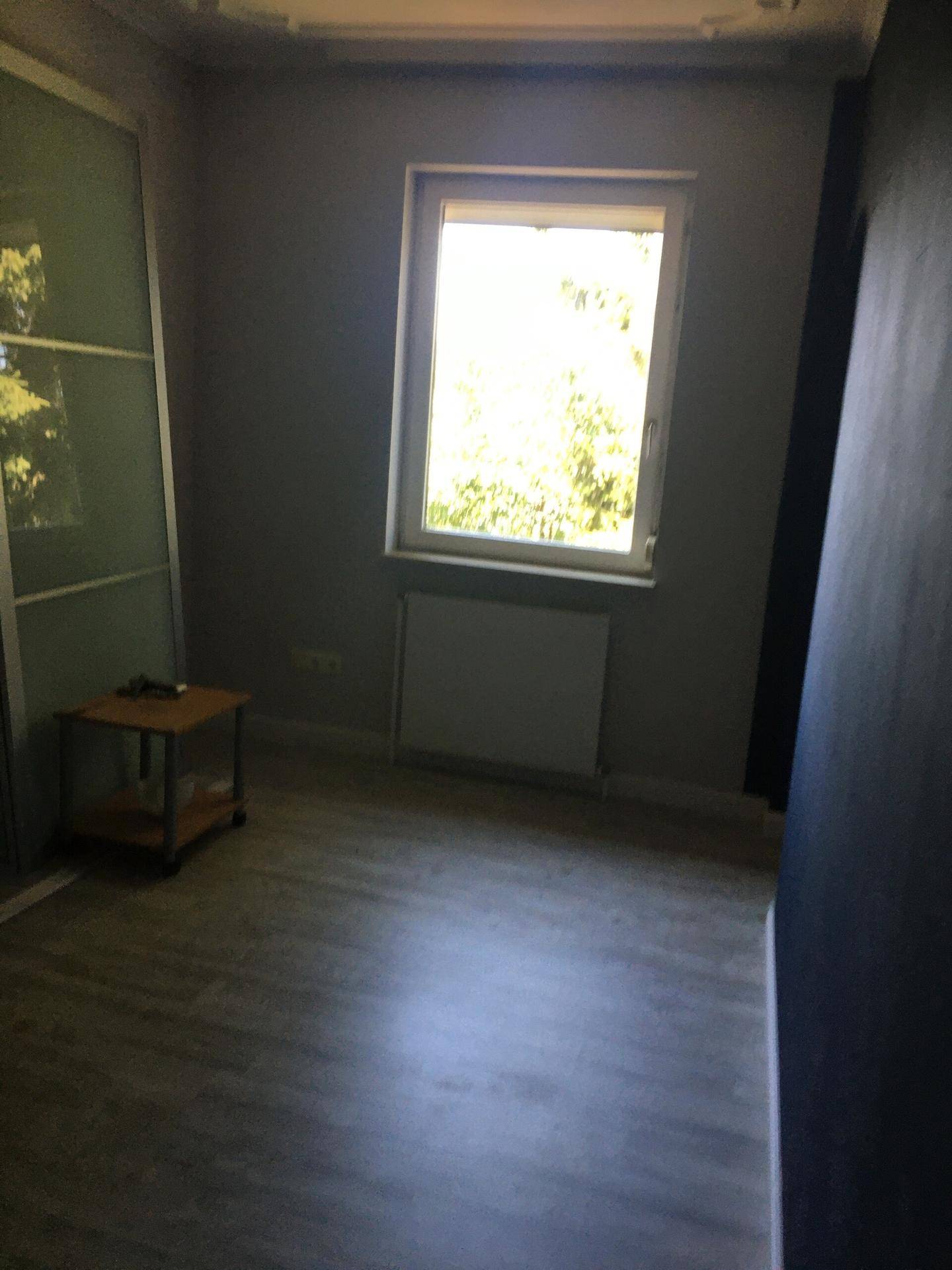 Leeres Schlafzimmer mit Laminatboden, Fenster und Schiebetürenschrank.