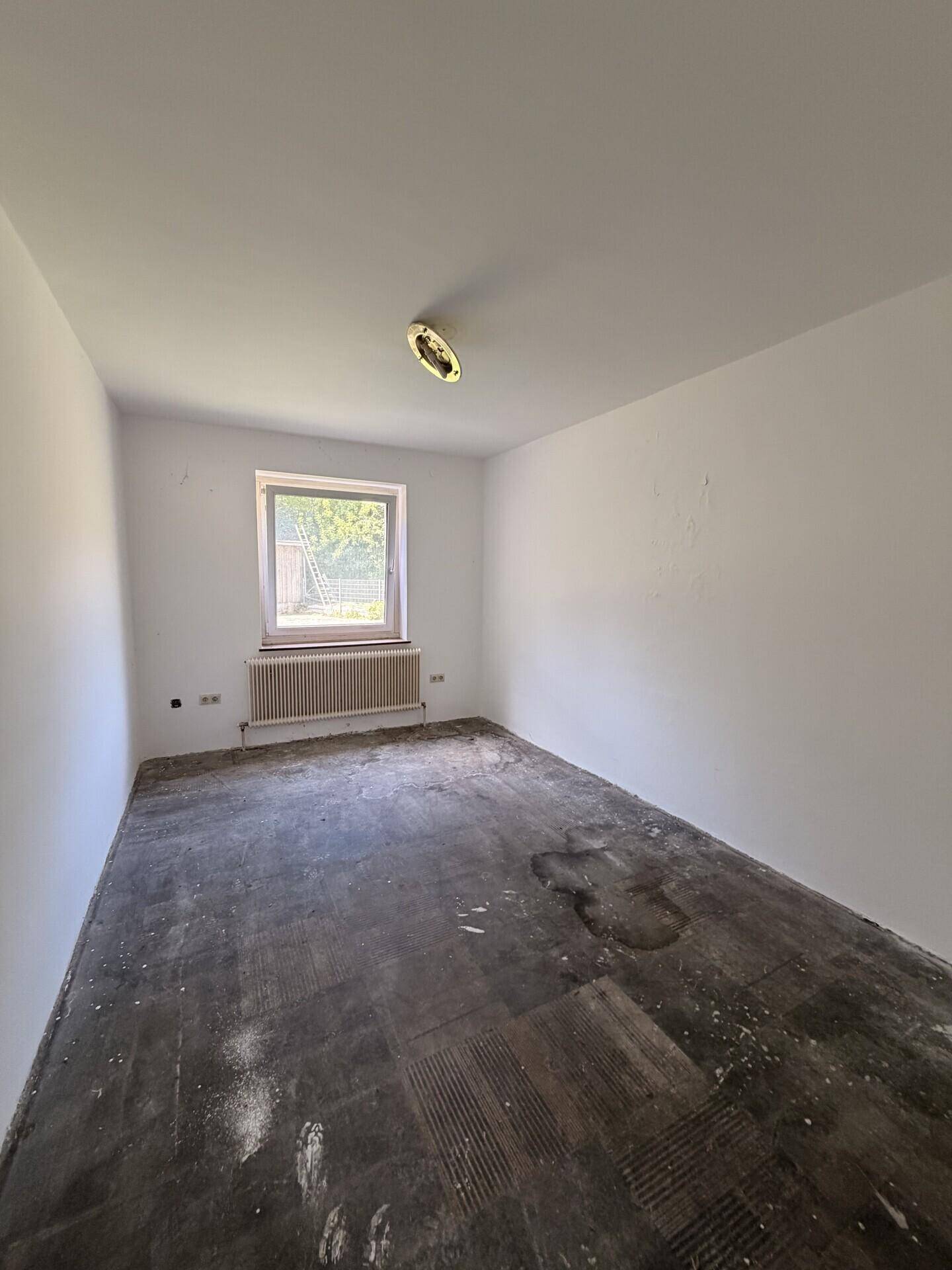 Helles Zimmer mit weiß gestrichenen Wänden und Rohboden, ideal für individuelle Gestaltung.