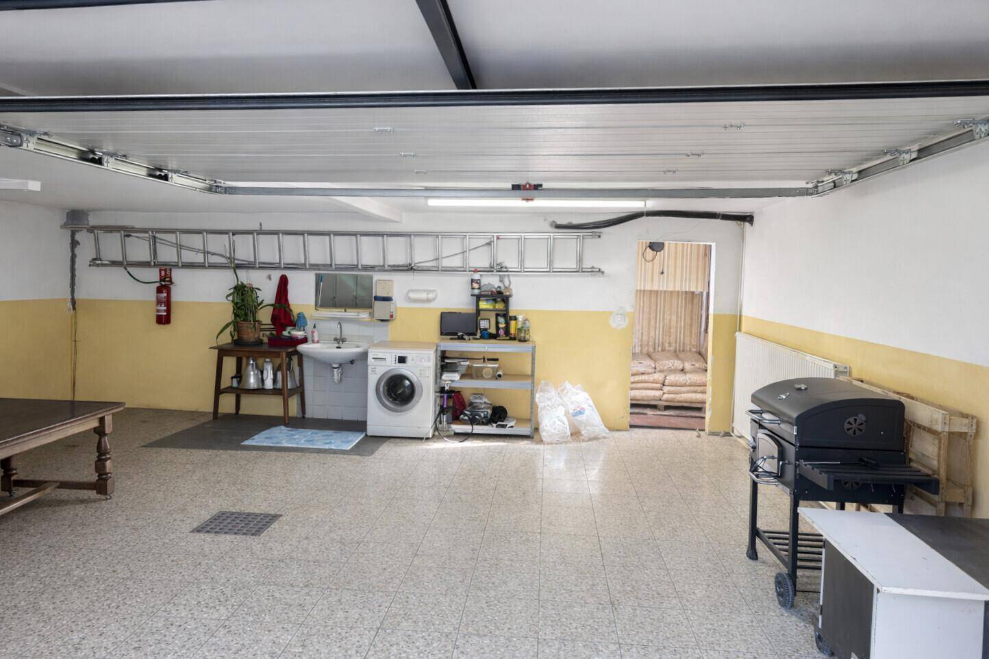 Geräumige Garage mit Waschmaschine, Spülbecken und Stauraum für verschiedene Gegenstände.