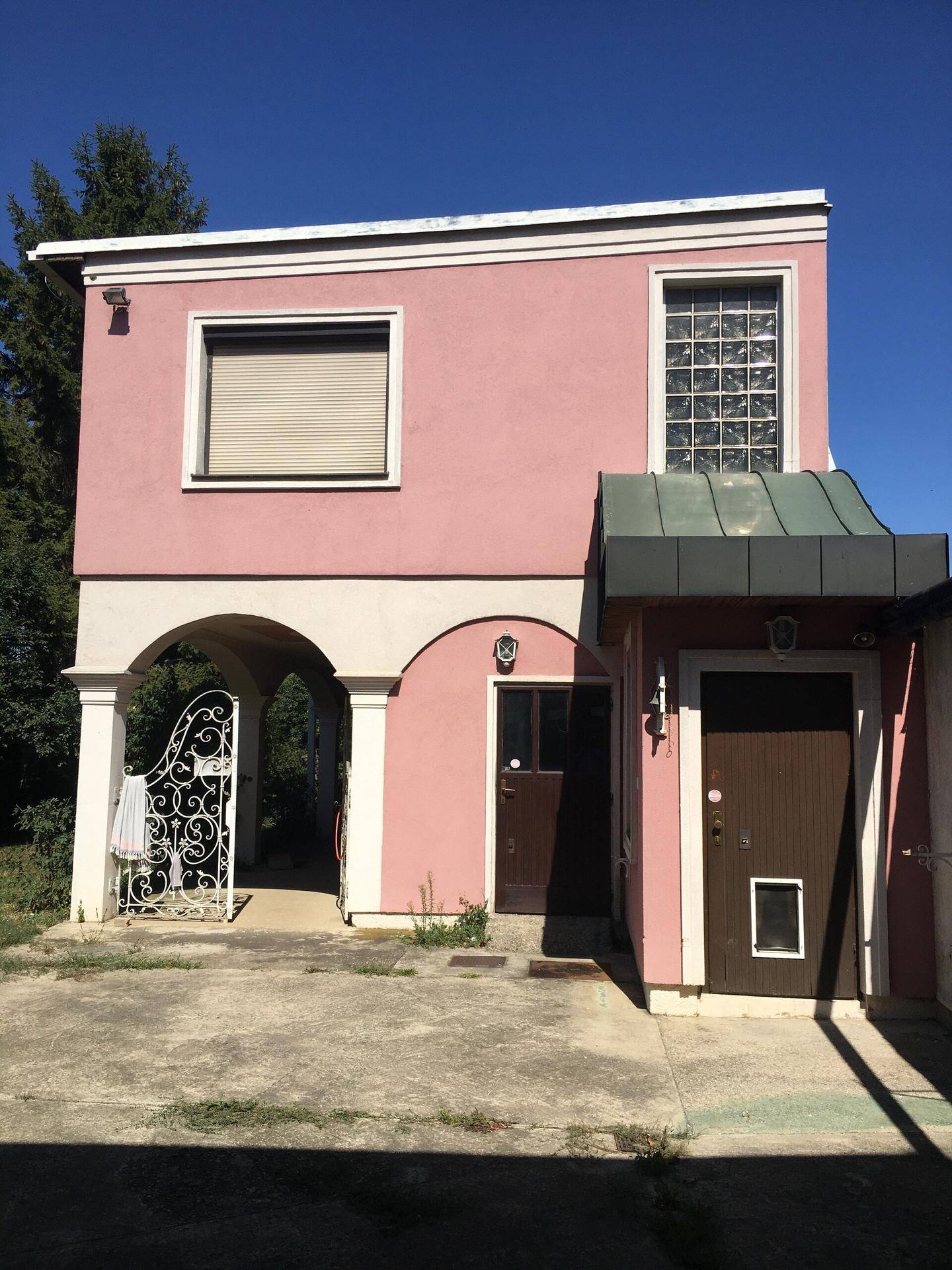 Vorderansicht des rosa Hauses mit Haupteingang und dekorativem Metalltor.