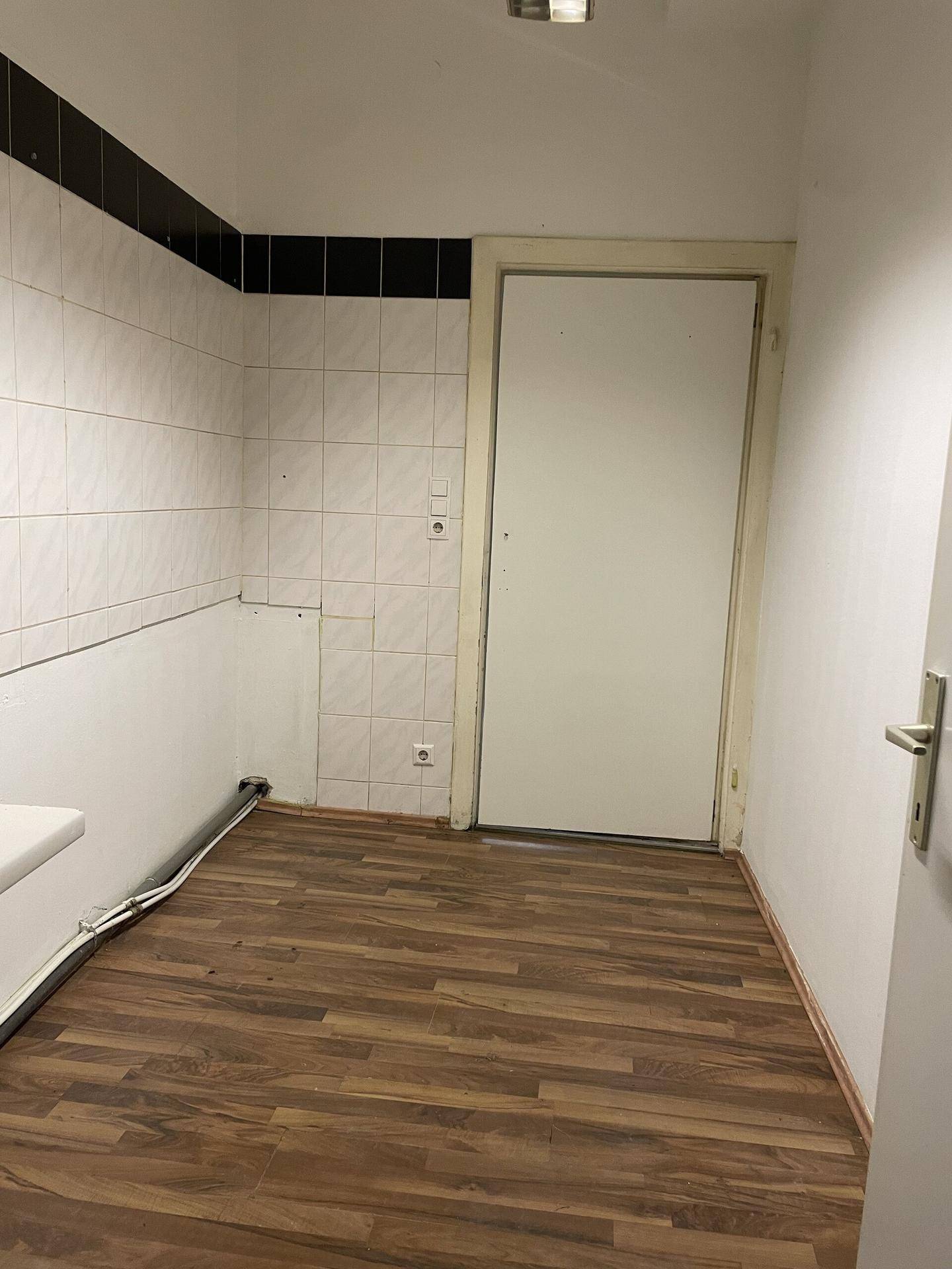 Einfacher Raum mit Laminatboden und teilweise gefliesten Wänden, ideal für eine kleine Küche oder Waschküche.