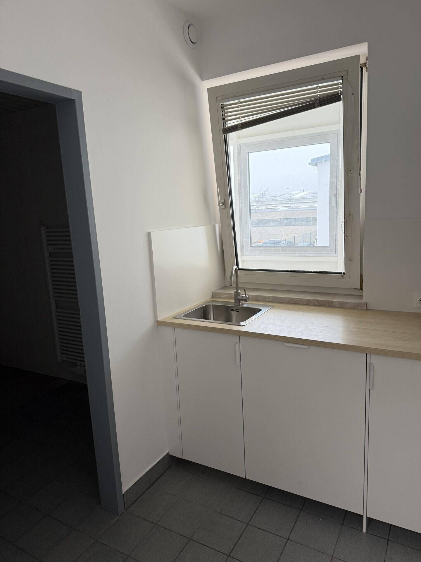 Kleine Küchenzeile mit weißen Schränken, einer Arbeitsplatte aus Holz und einer Spüle unter einem Fenster.