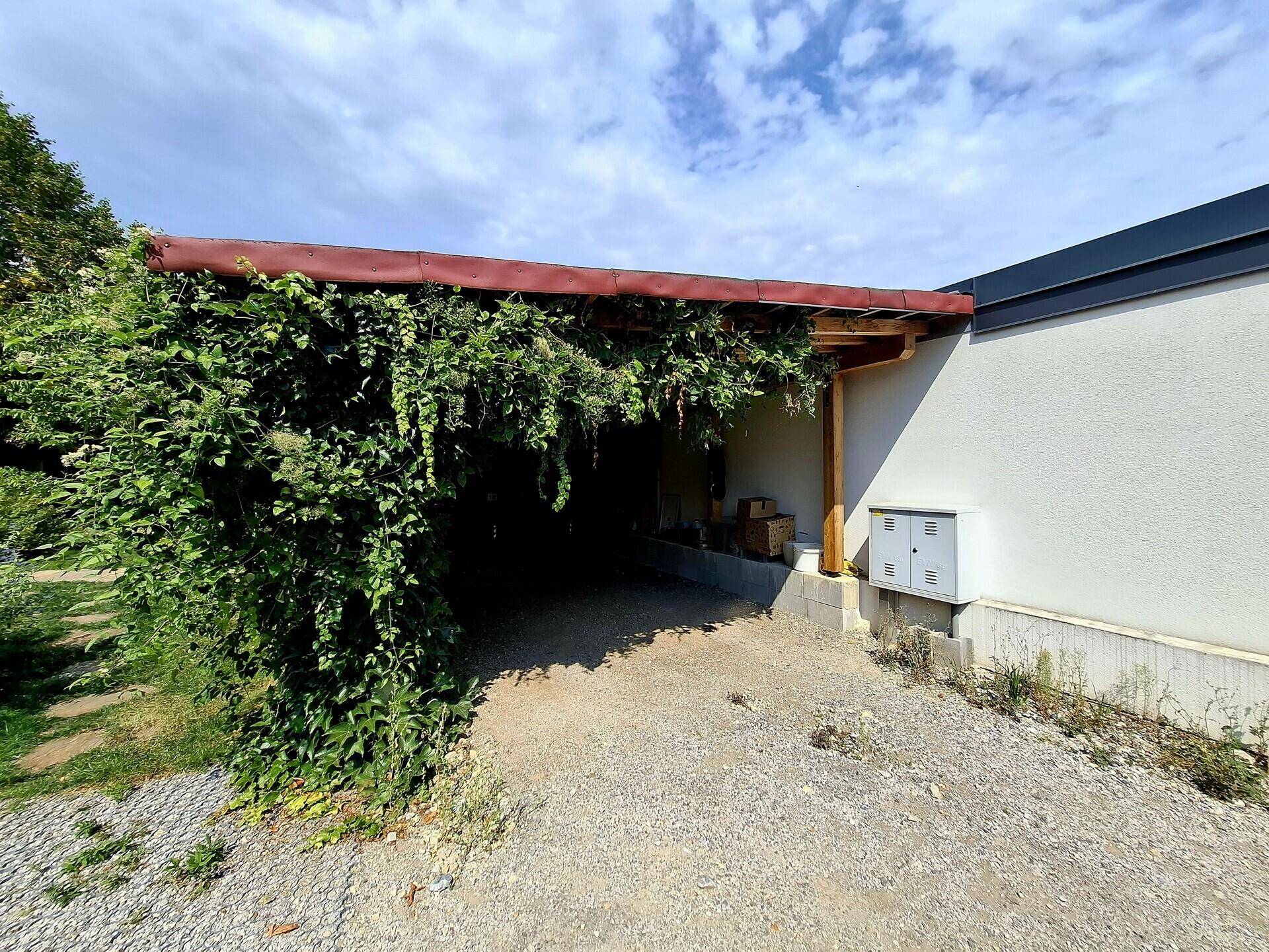 Überdachter Carport, umgeben von üppigem Grün, bietet Schutz für Fahrzeuge.