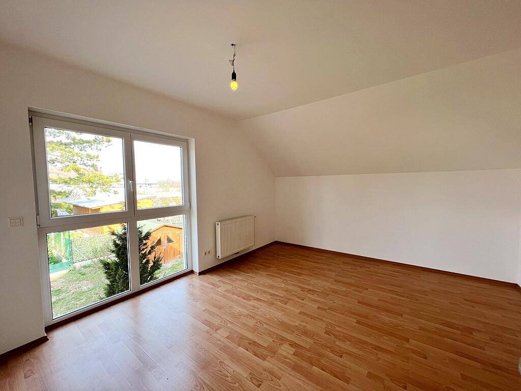 Helles Schlafzimmer mit Laminatboden, großem Fenster und Dachschräge, bietet Blick ins Grüne.