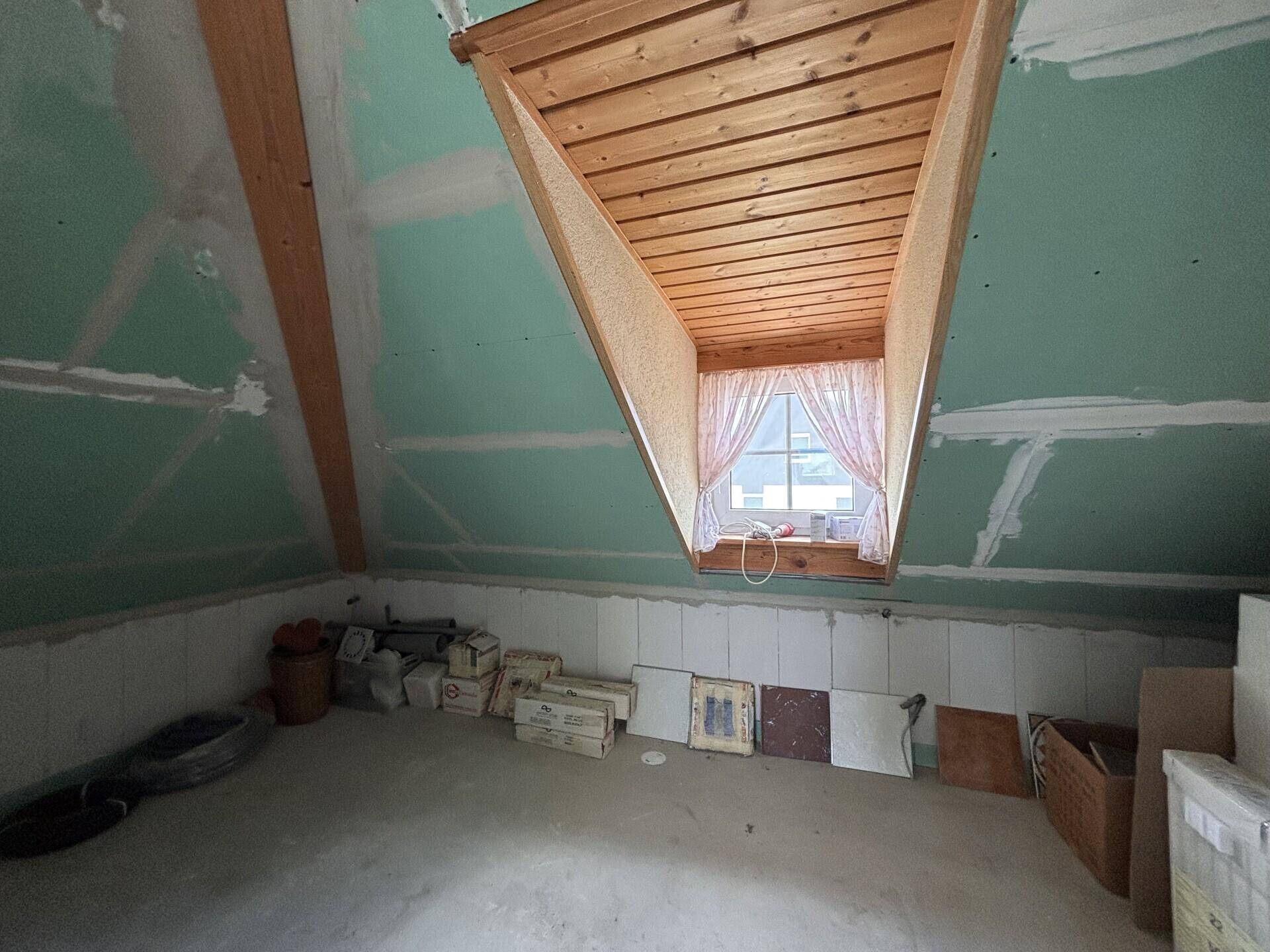 Dachgeschossraum im Rohbau mit Dachfenster und Blick nach draußen, bereit zum Ausbau.