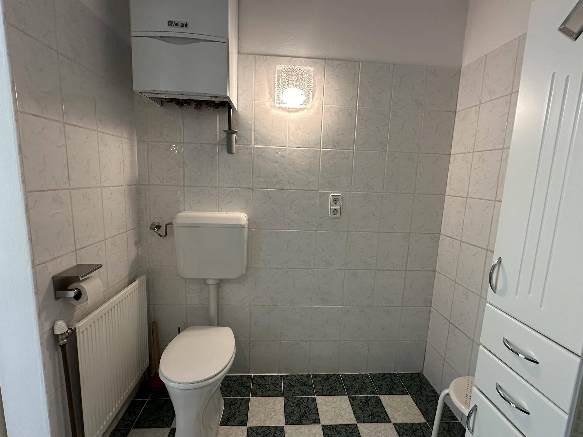 Separates WC mit Toilette, Heizkörper und Wandfliesen.