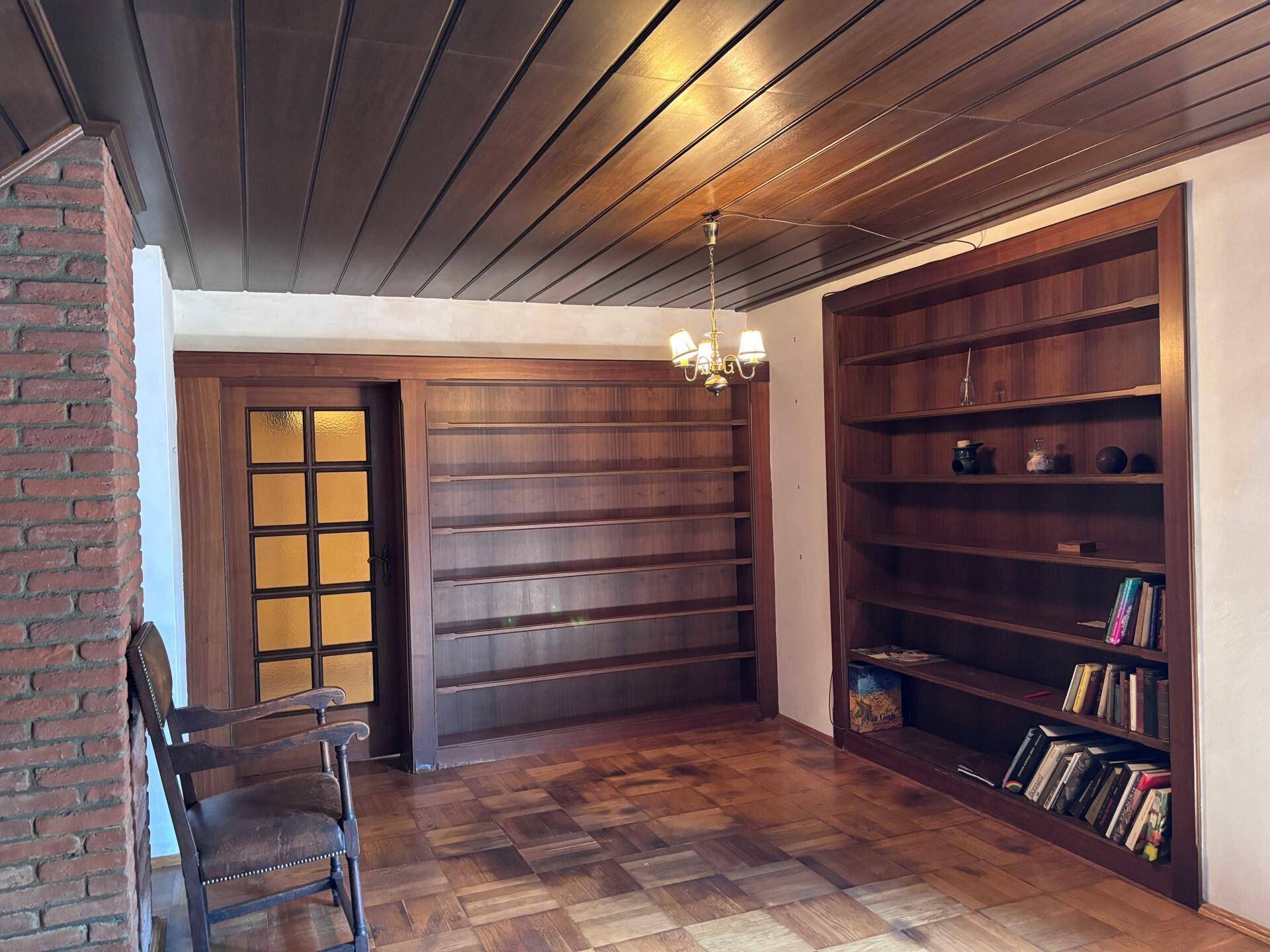 Zimmer mit Holzboden, Holzbalkendecke und großen eingebauten Bücherregalen.