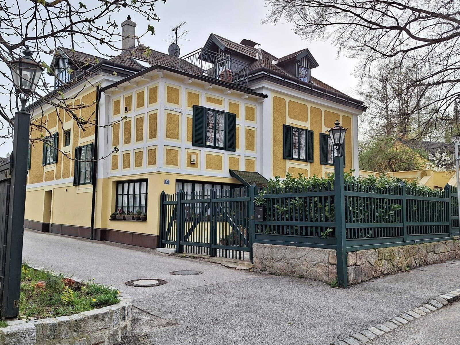 Charmantes Gebäude mit gelber Fassade, grünen Fensterläden und gepflegtem Zaun.