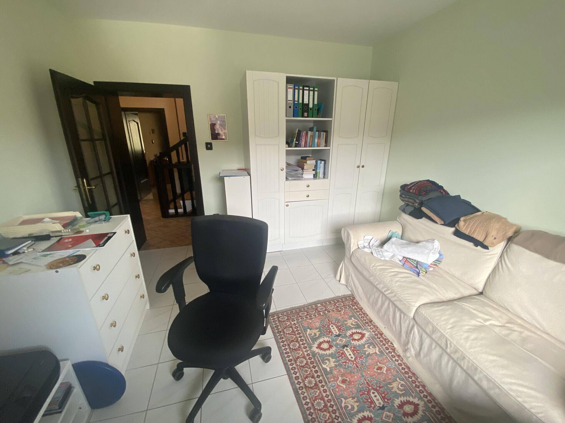 Helles Arbeitszimmer mit Schreibtisch, Regal und Sofa, ideal für Home-Office.