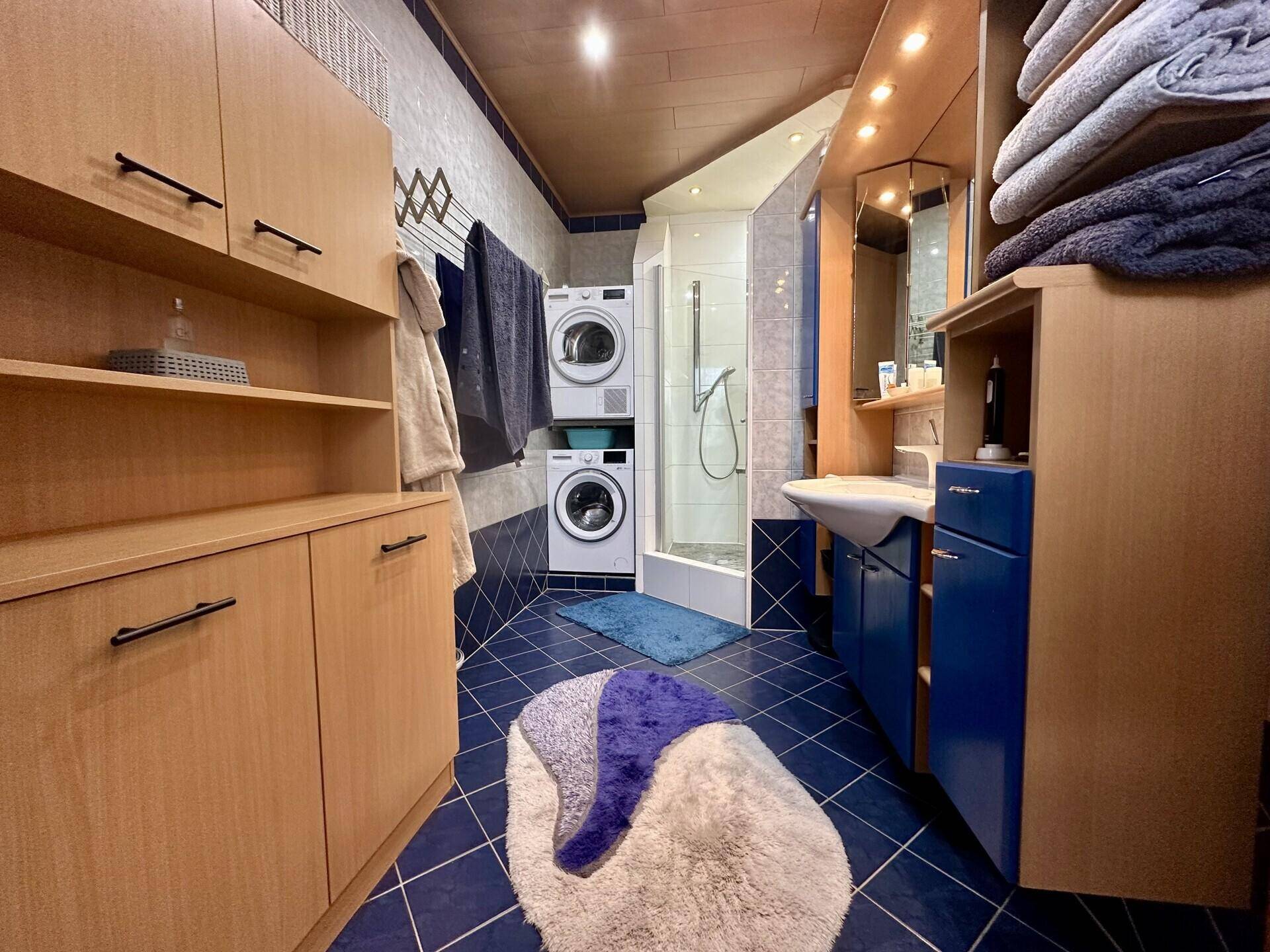 Badezimmer mit blauen Fliesen, Duschkabine, Waschbecken und Waschmaschine sowie Trockner.
