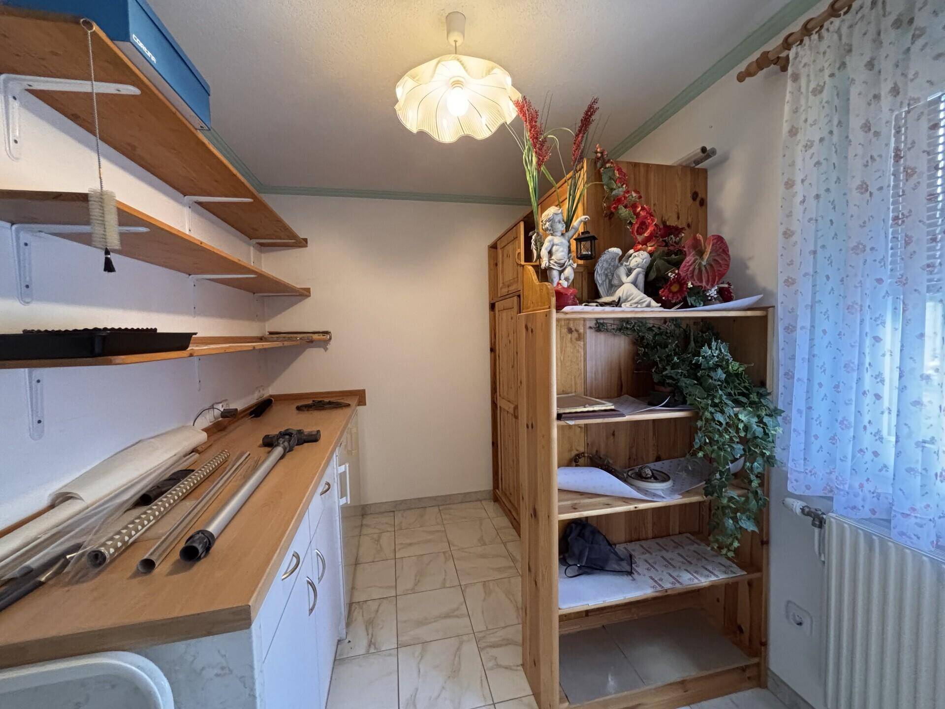 Praktischer Abstellraum mit offenen Holzregalen, Arbeitsplatte und gefliestem Boden.