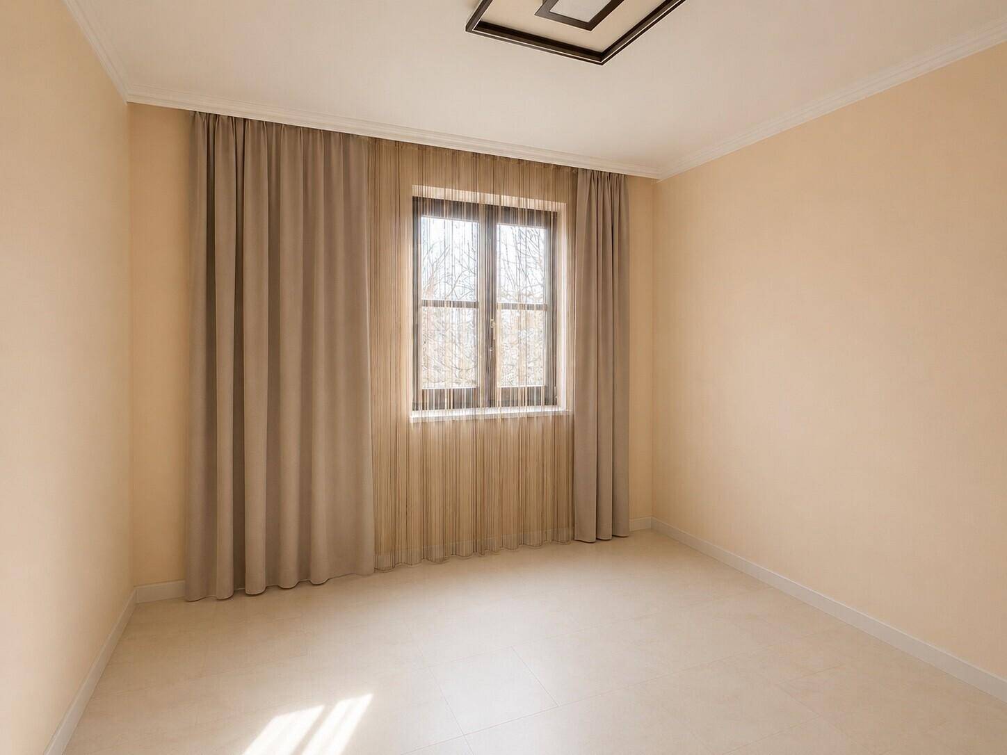 Ruhiges Zimmer mit beigefarbenen Wänden, Fliesenboden und einem Fenster mit Vorhängen.