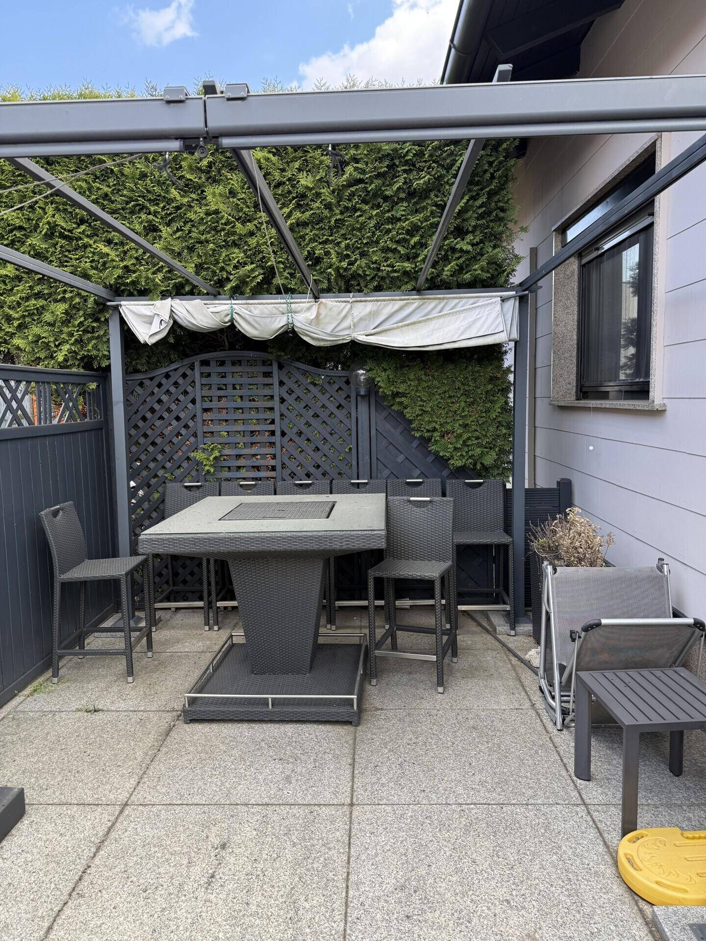 Überdachte Terrasse mit Gartenmöbeln und Sichtschutzhecke, ideal für Mahlzeiten im Freien.