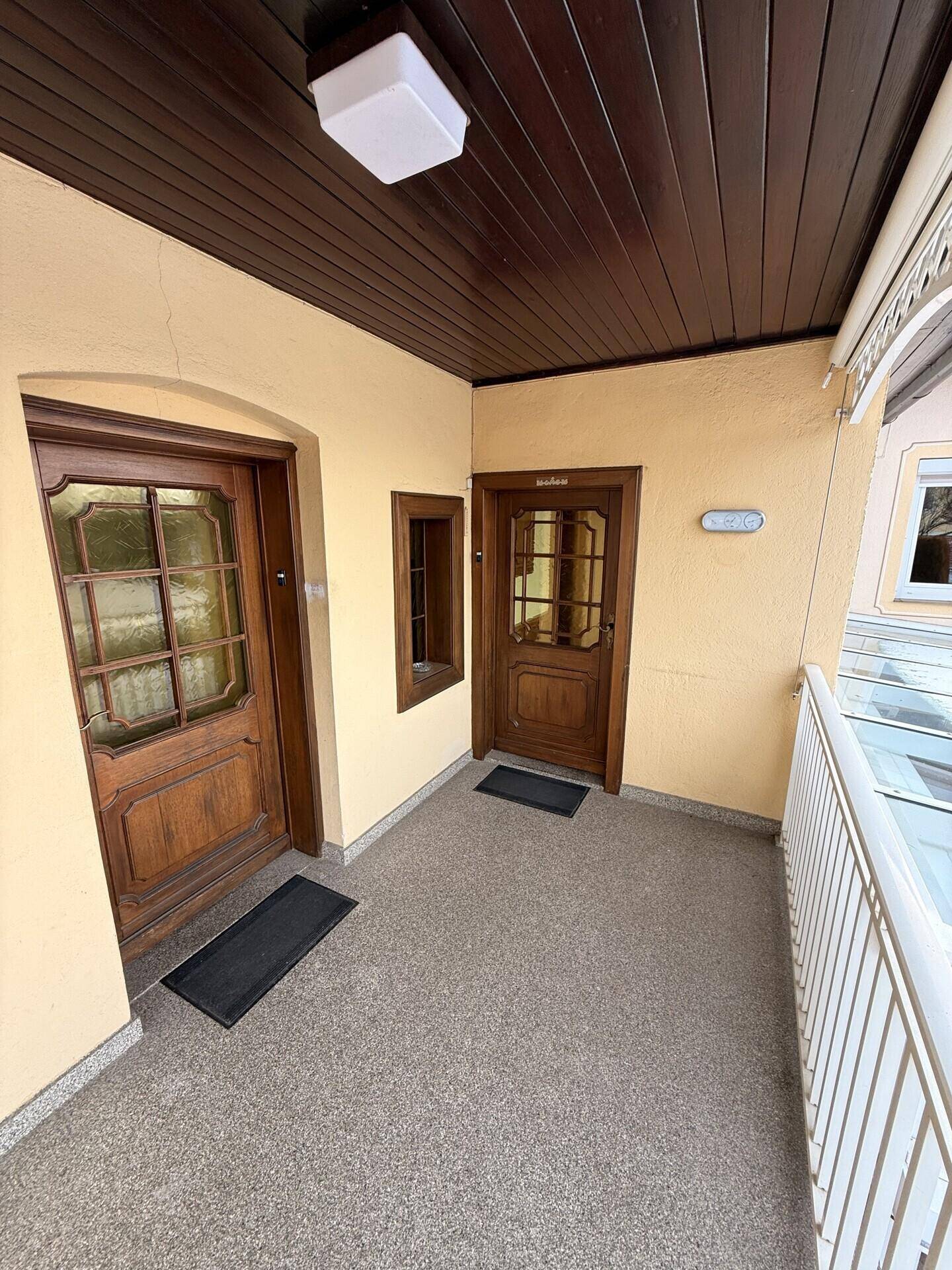 Eingangsbereich mit zwei Holztüren auf einem überdachten Balkon.