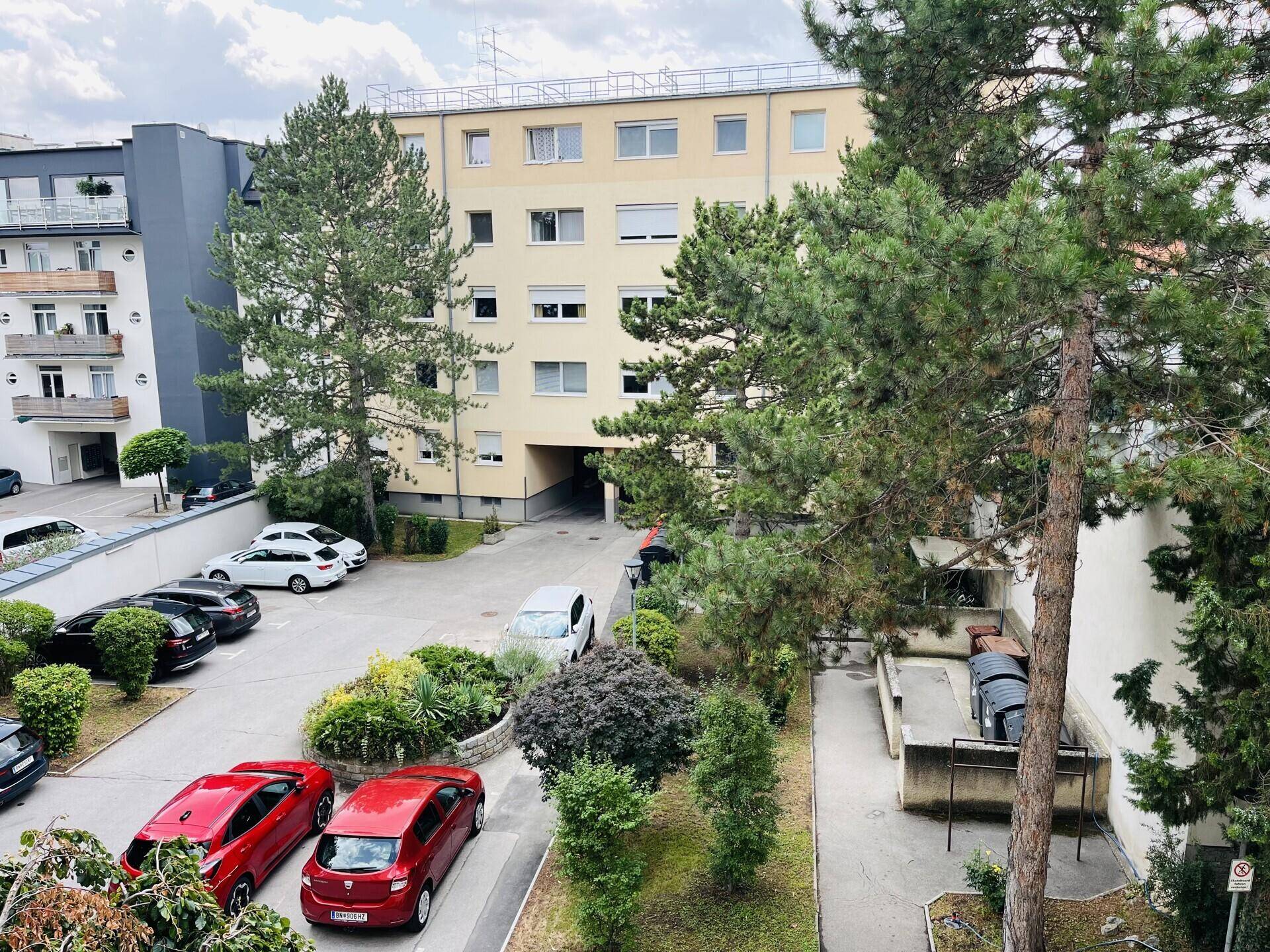 Außenansicht des Gebäudes mit Parkplätzen und Bäumen im Hofbereich.