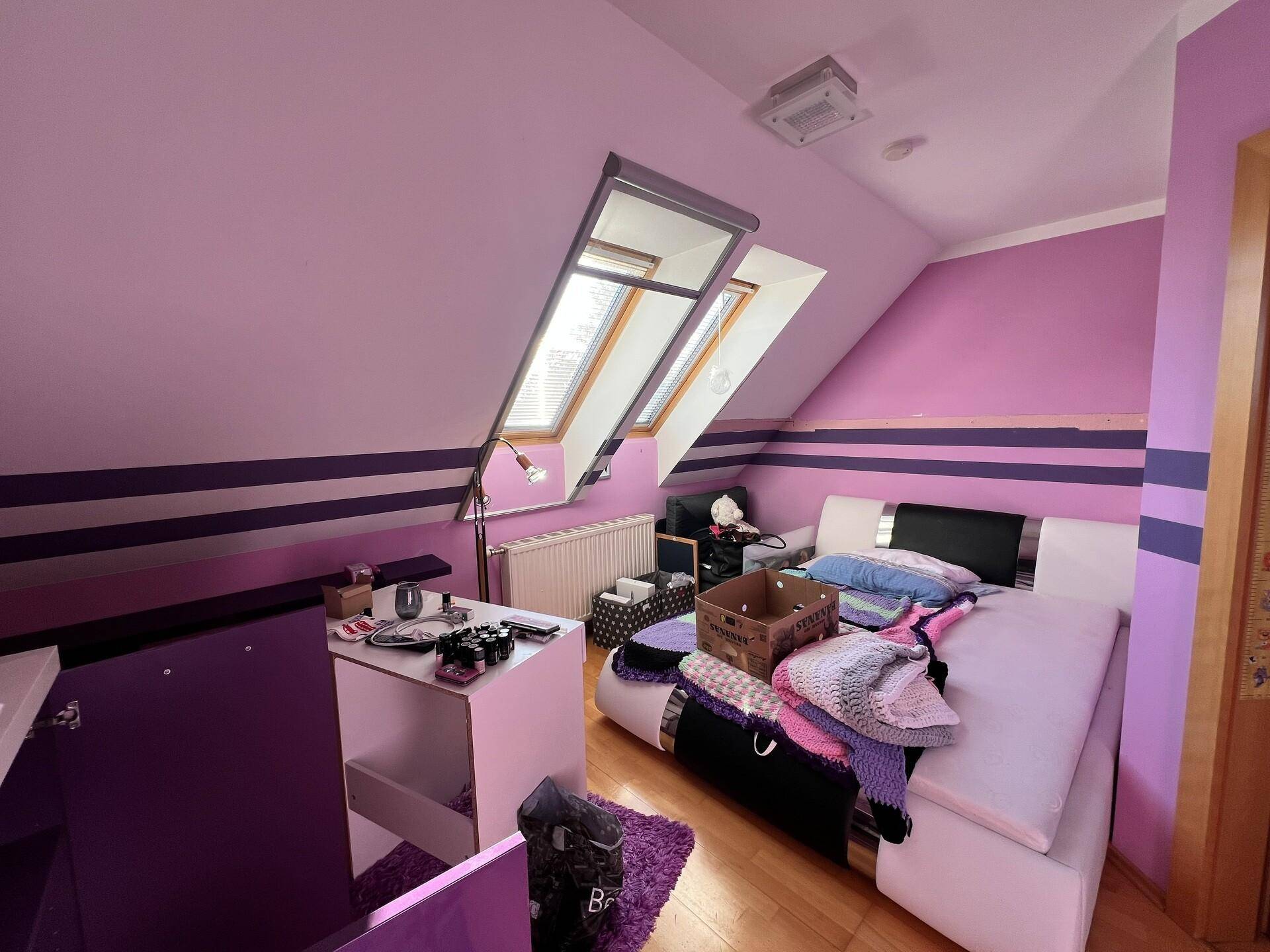 Dachgeschoss-Schlafzimmer mit lila Wänden, Holzboden und Dachfenstern.