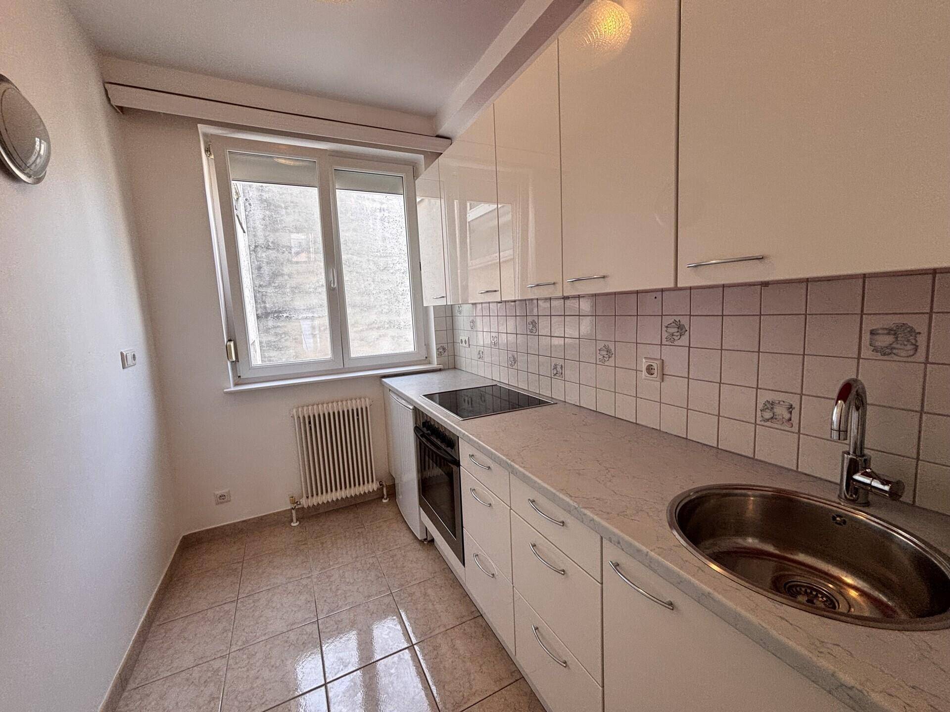 Funktionale Küche mit weißen Hochglanzschränken, Fliesenboden und Fenster für Tageslicht.