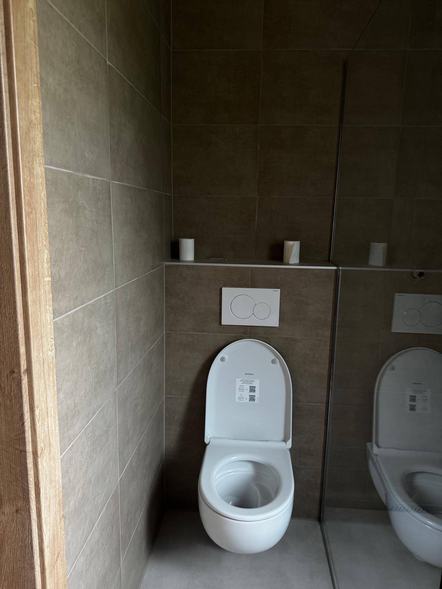 Modernes WC mit wandhängender Toilette, braun-grauen Fliesen und einem Spiegel.