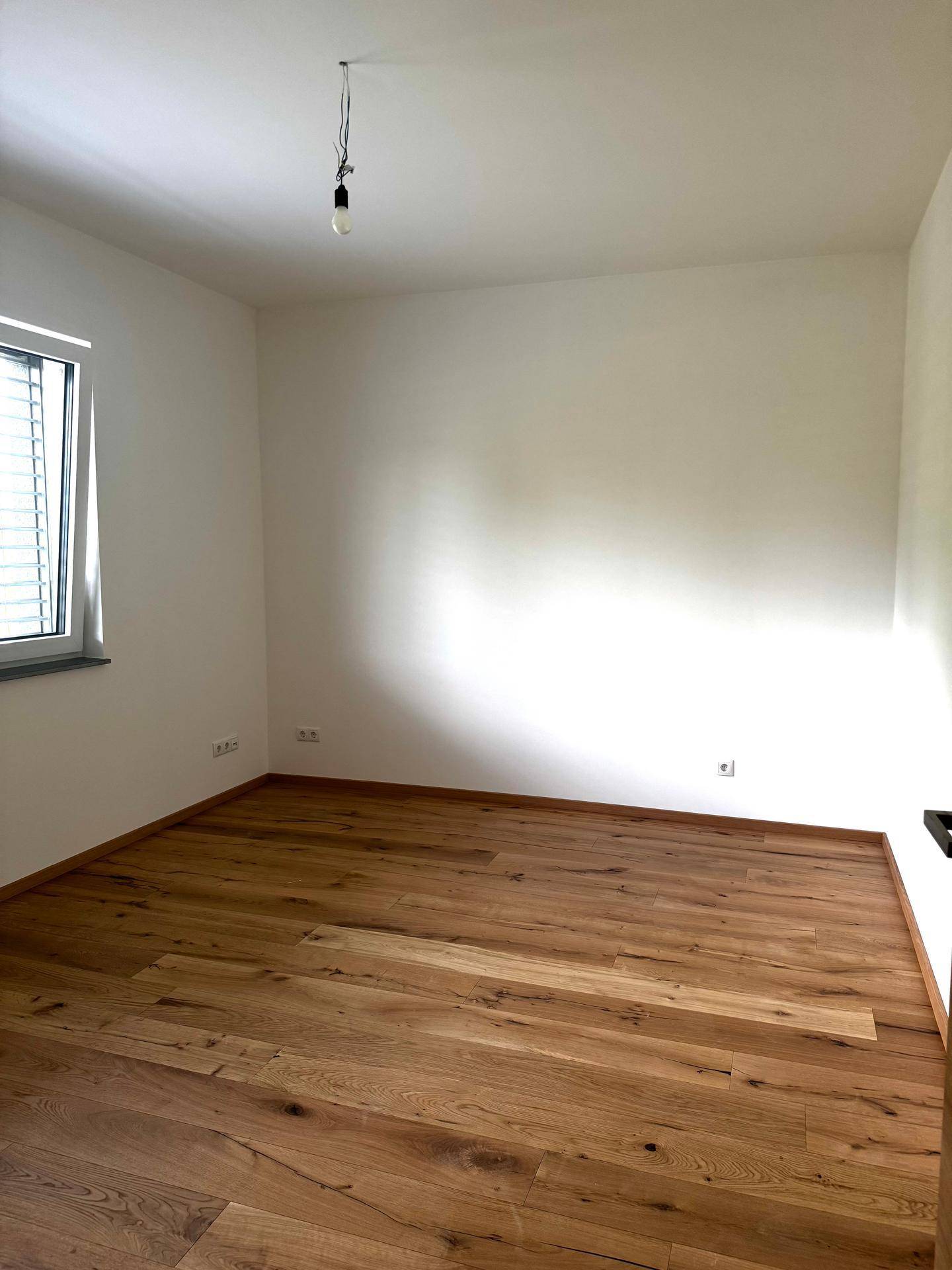 Helles Schlafzimmer mit neuem Holzboden, weißen Wänden und einem Fenster mit Jalousien.
