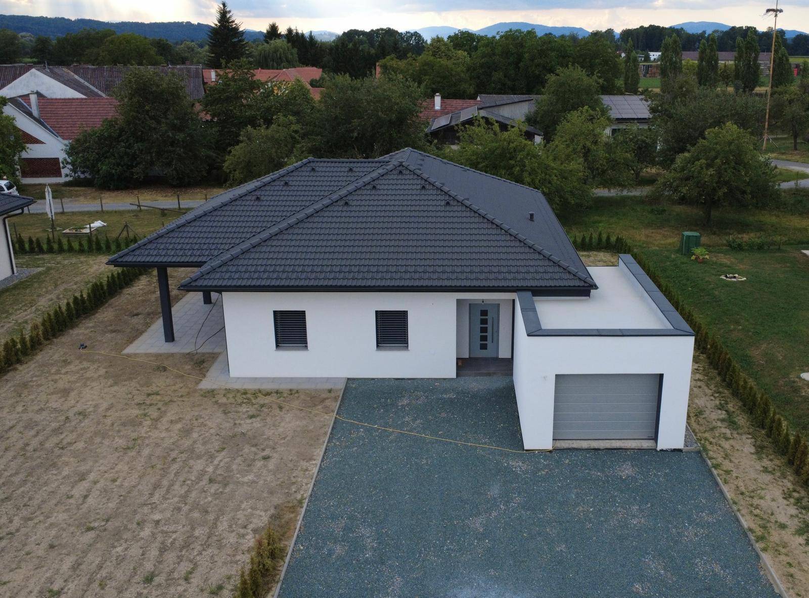Modernes Einfamilienhaus mit Satteldach und Flachdach-Anbau für die Garage, umgeben von Grünflächen.