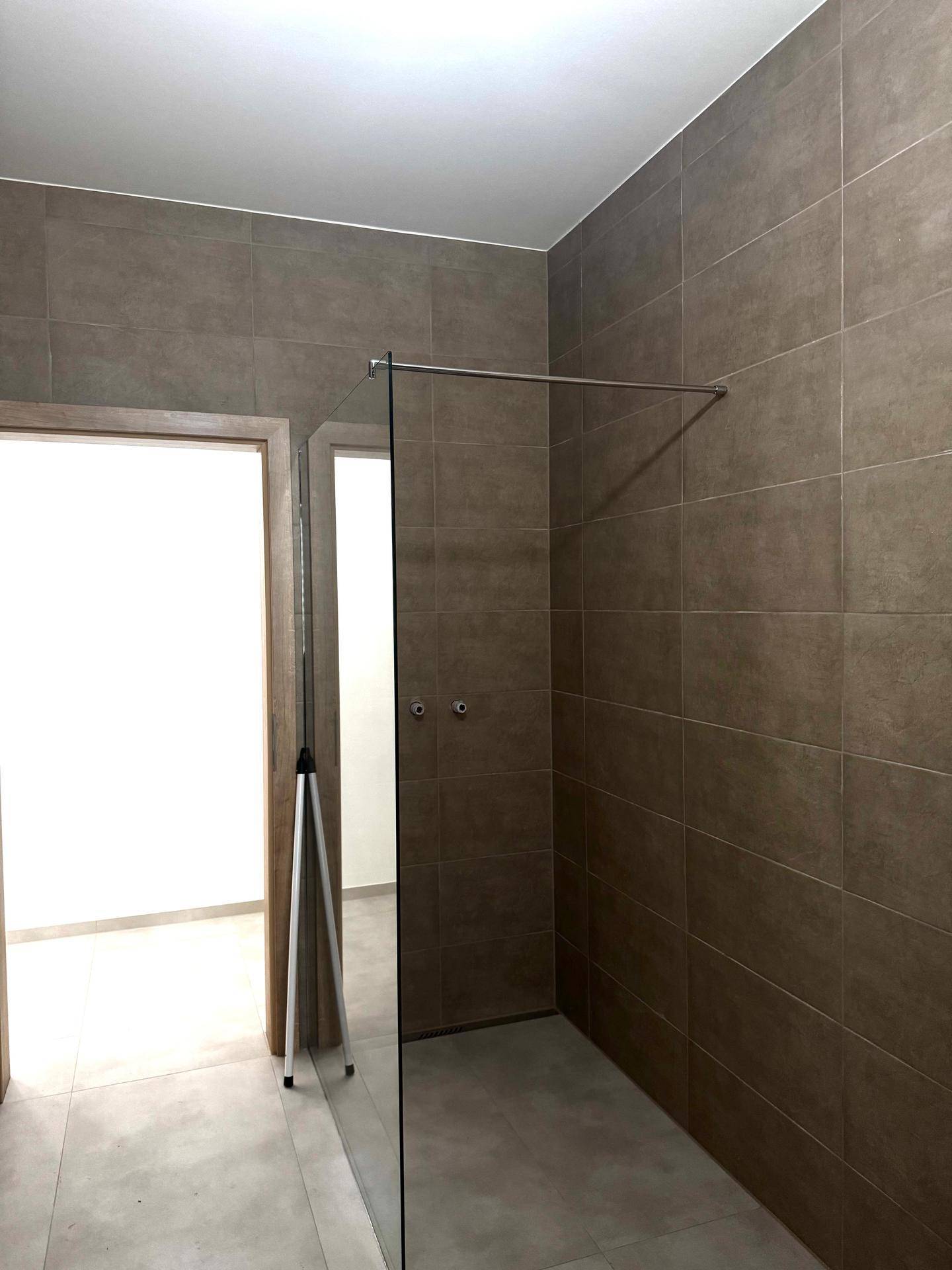 Moderne Duschkabine mit Glasabtrennung und braun-grauen Fliesen im Badezimmer.
